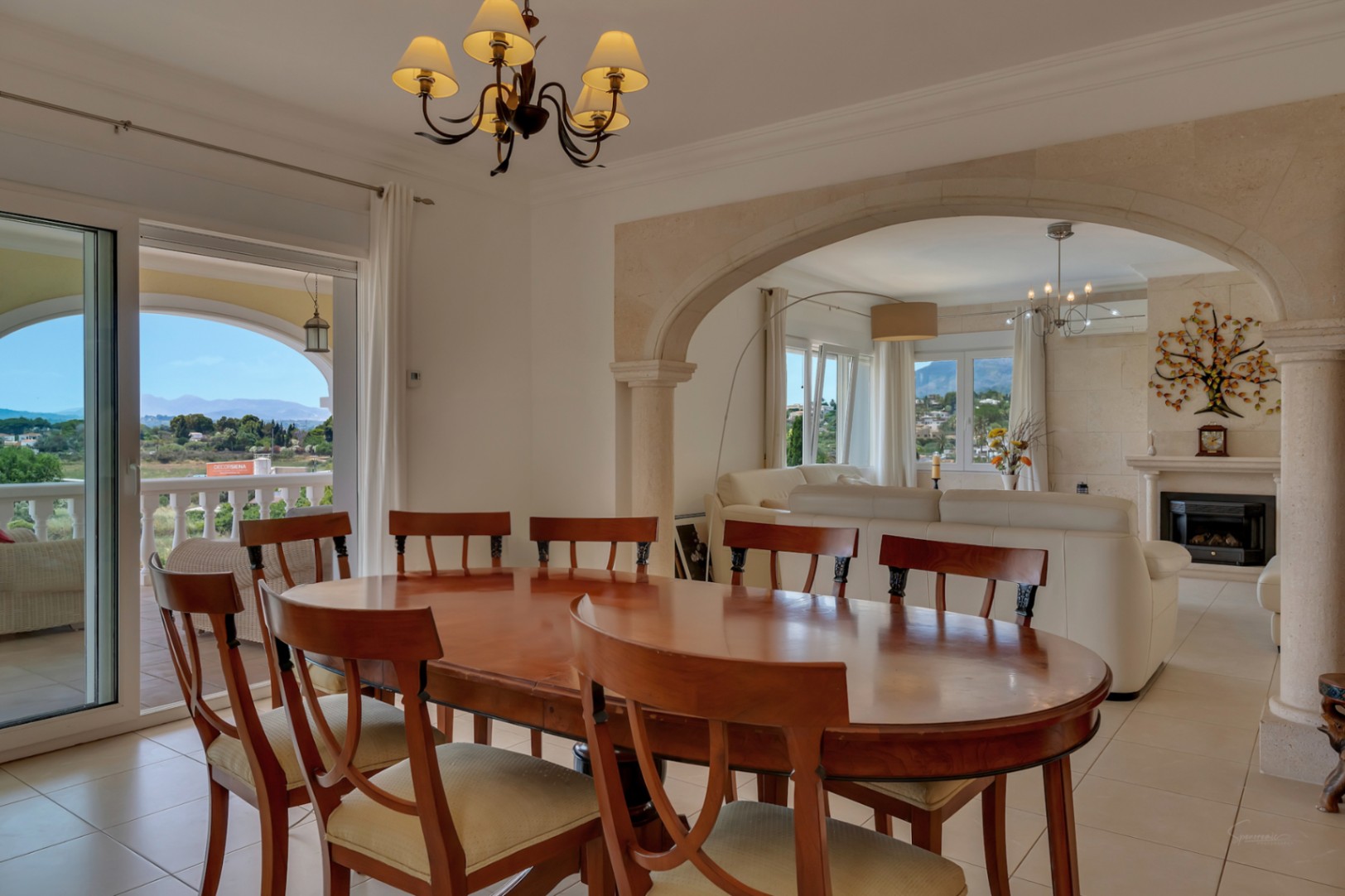 Comedor con mesa de madera noble conectado al salón mediante un arco de piedra tosca, con acceso directo a la naya y vistas panorámicas al valle.