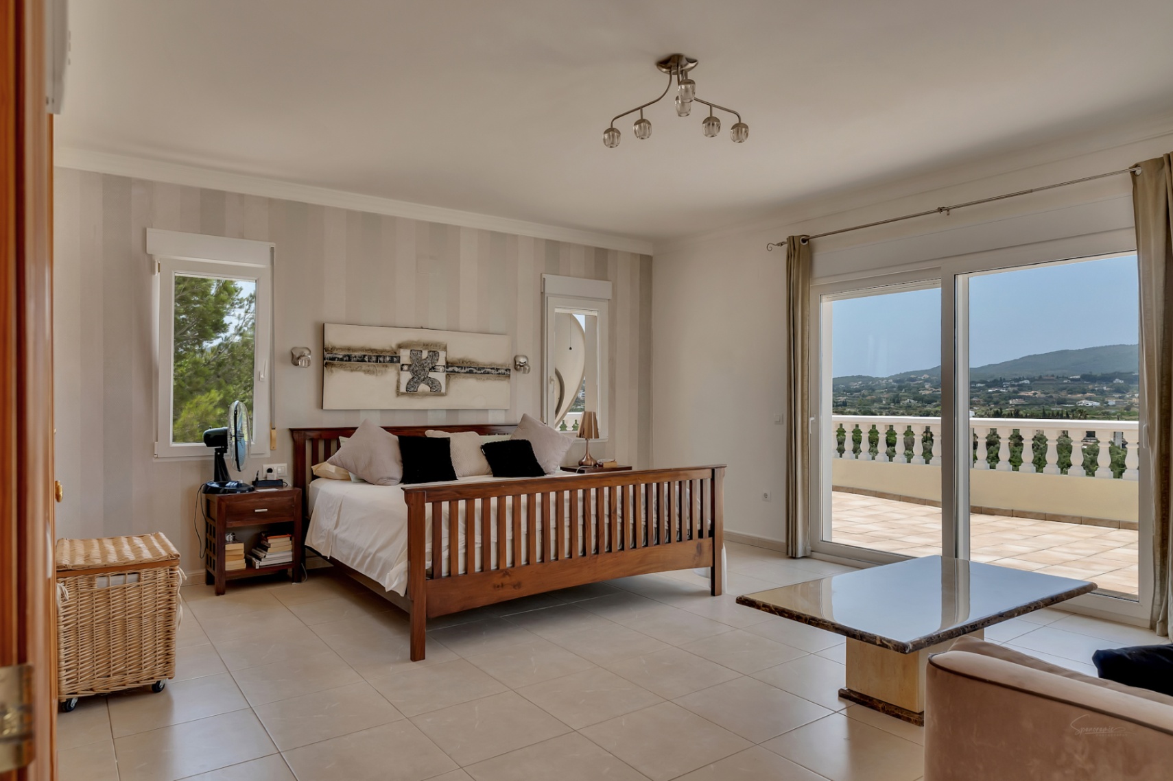 Dormitorio principal con cama de madera, papel pintado a rayas y acceso directo a una terraza privada con vistas panorámicas al valle y balaustrada clásica.