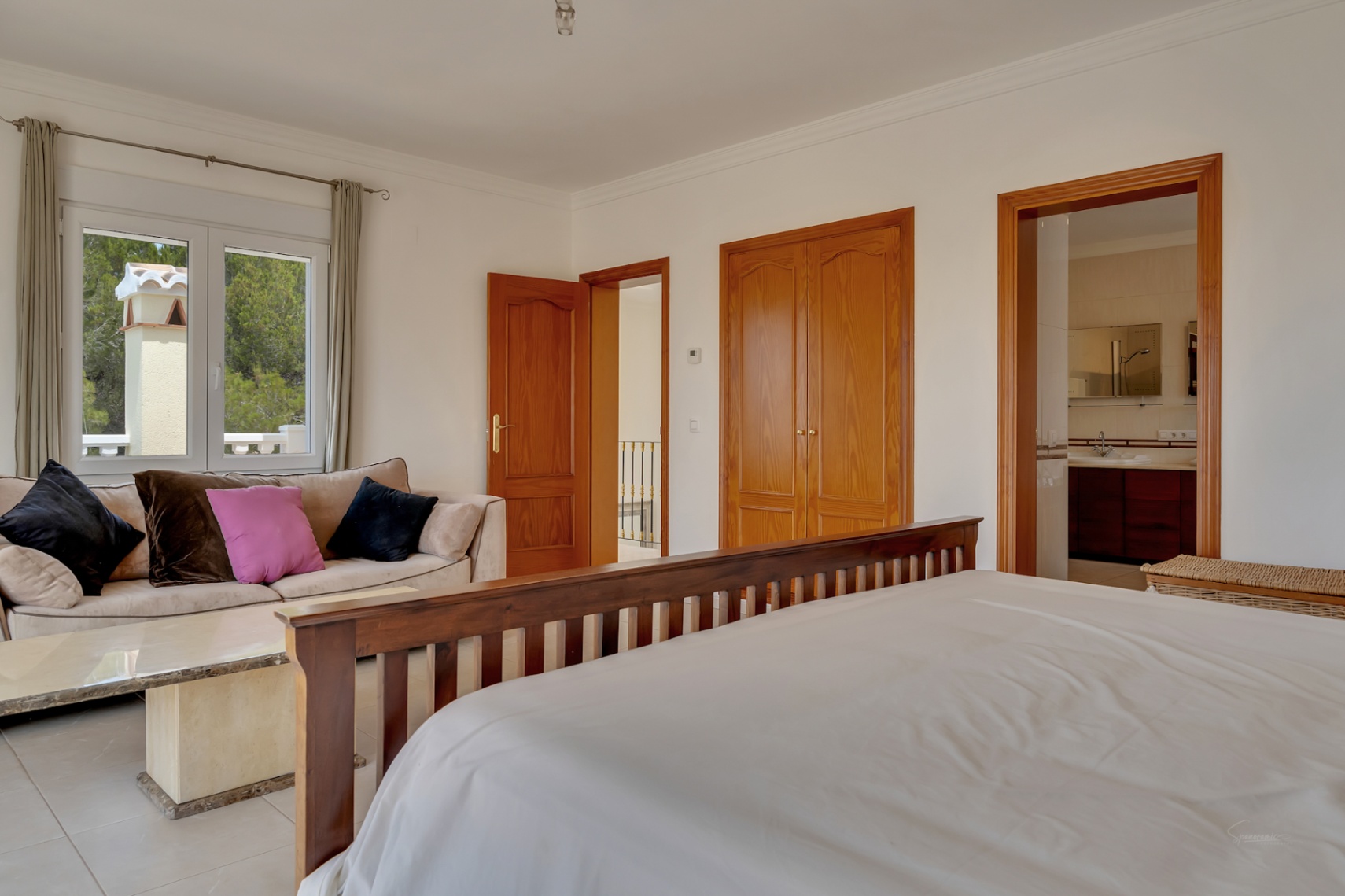 Dormitorio principal con zona de estar, armarios empotrados de madera y baño en suite. Dispone de ventanales que ofrecen vistas al entorno natural.