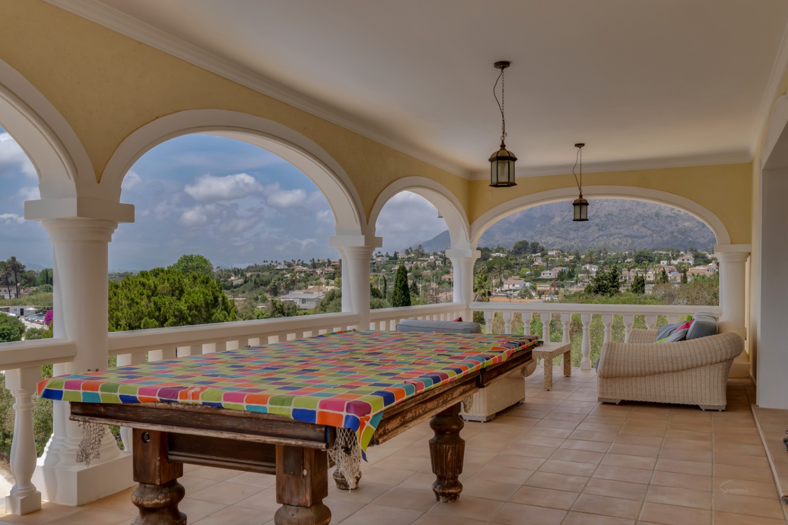 Naya cubierta con arcos clásicos y columnas blancas, equipada con mesa de billar y zona de estar, con vistas panorámicas al Montgó y al valle de Jávea.