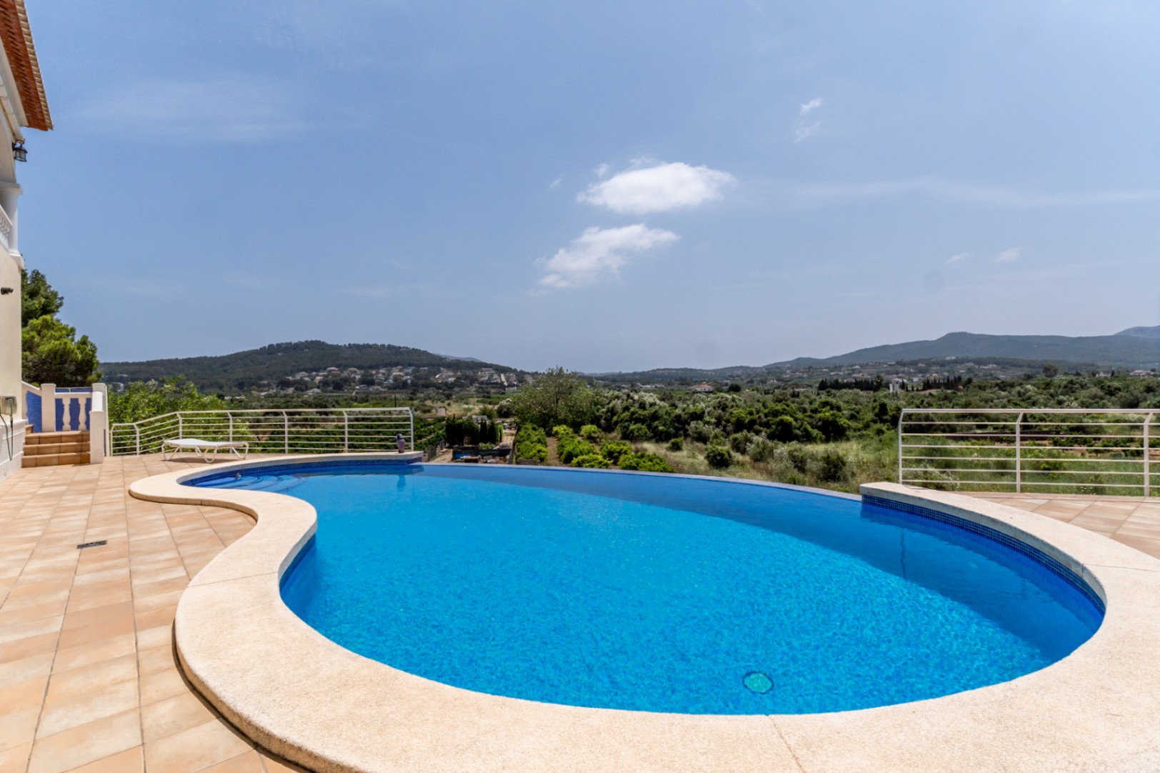 Piscina infinity de diseño curvo con vistas panorámicas al valle de Jávea, rodeada de una amplia terraza de gres y barandillas metálicas blancas.