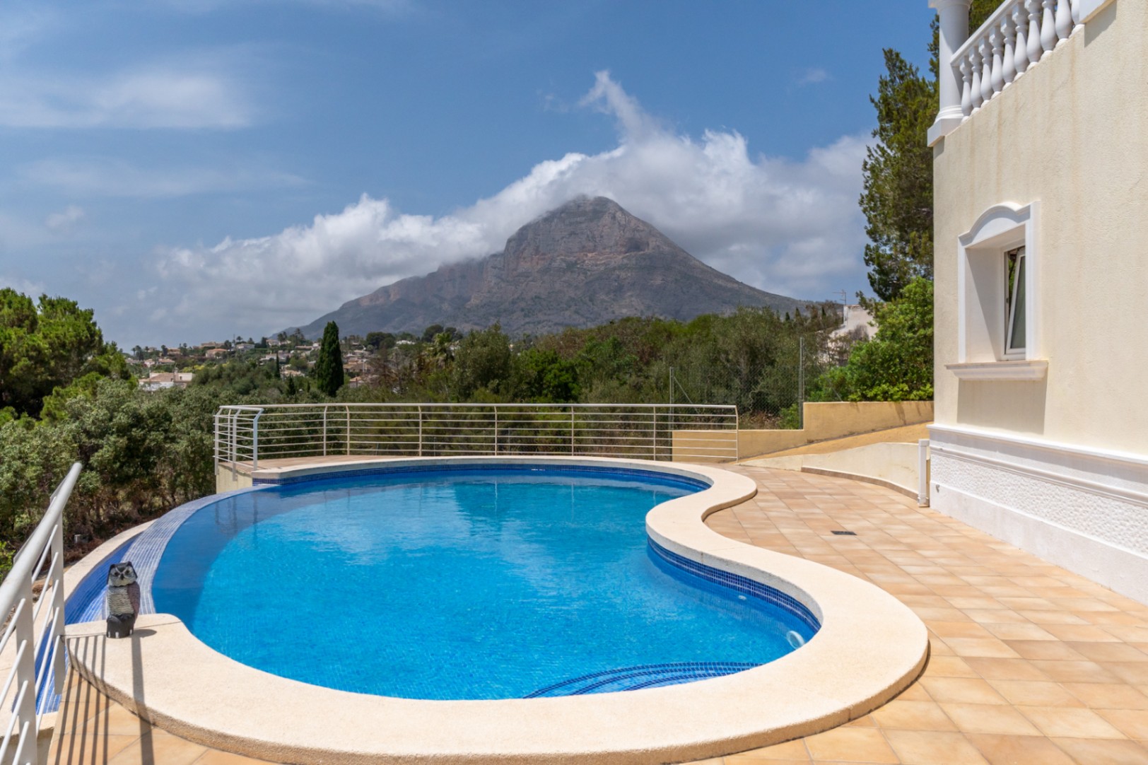 Piscina infinity de forma curva con vistas panorámicas al valle y al macizo del Montgó, rodeada por una amplia terraza de gres y barandilla de seguridad.