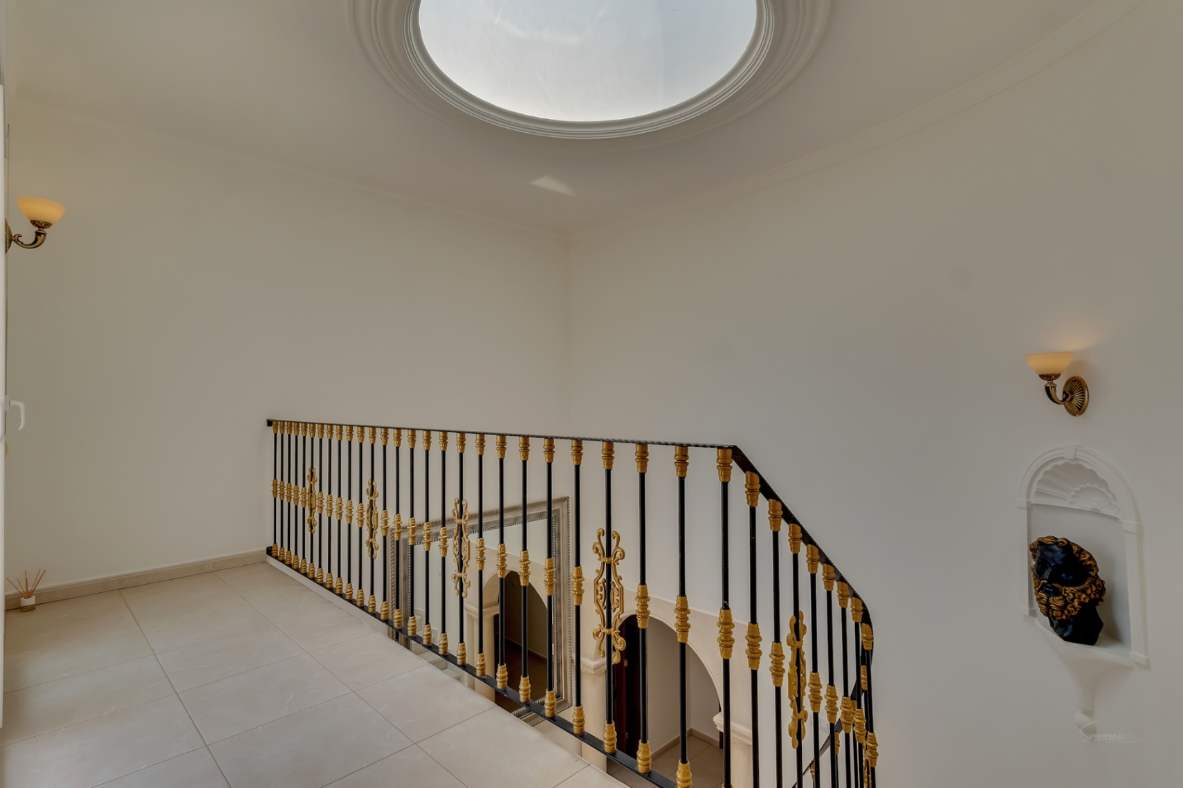 Rellano superior con cúpula acristalada, barandilla de hierro forjado con detalles dorados y hornacina decorativa. Vista al hall de entrada de doble altura.