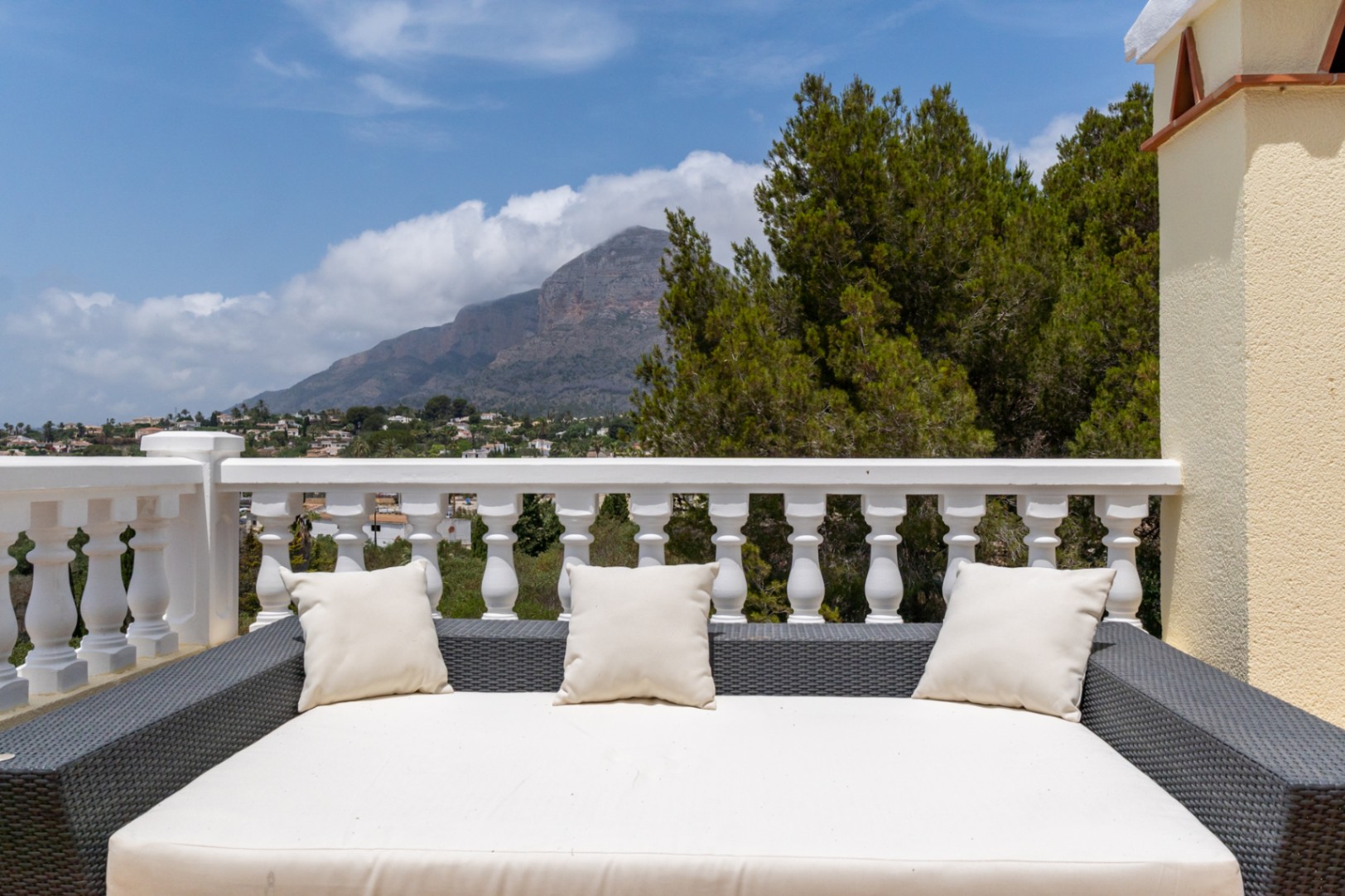 Terraza superior con cama de exterior de ratán y vistas panorámicas directas al Montgó y al valle, delimitada por una balaustrada blanca clásica.