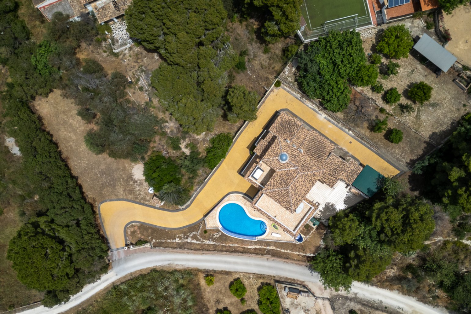 Vista aérea cenital de la villa que muestra la distribución de la parcela, el tejado con cúpula central, el camino de acceso curvo y la piscina integrada.