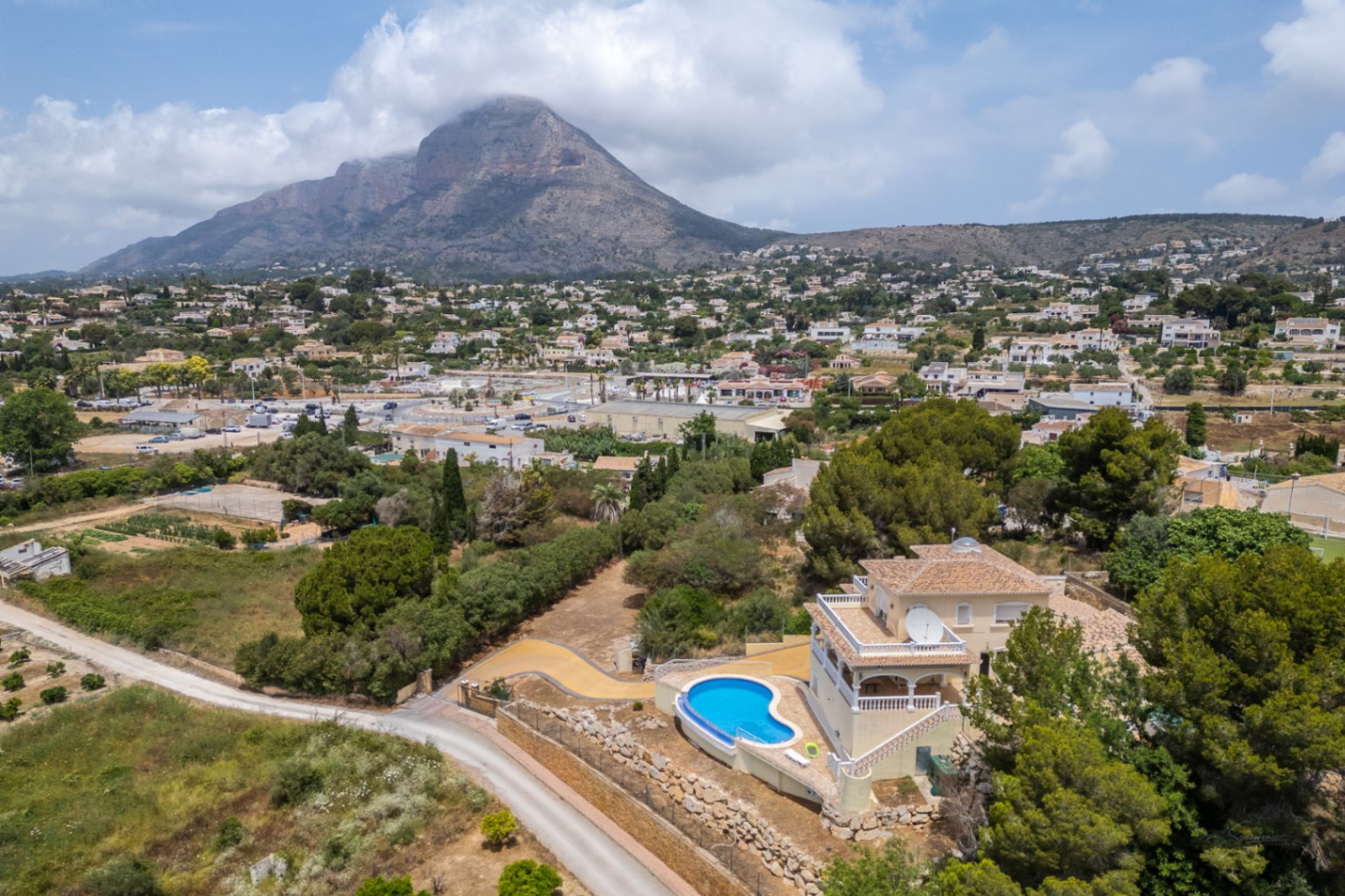 Vista aérea de la villa que destaca la piscina curva elevada y las terrazas orientadas hacia el valle, con el macizo del Montgó dominando el horizonte.