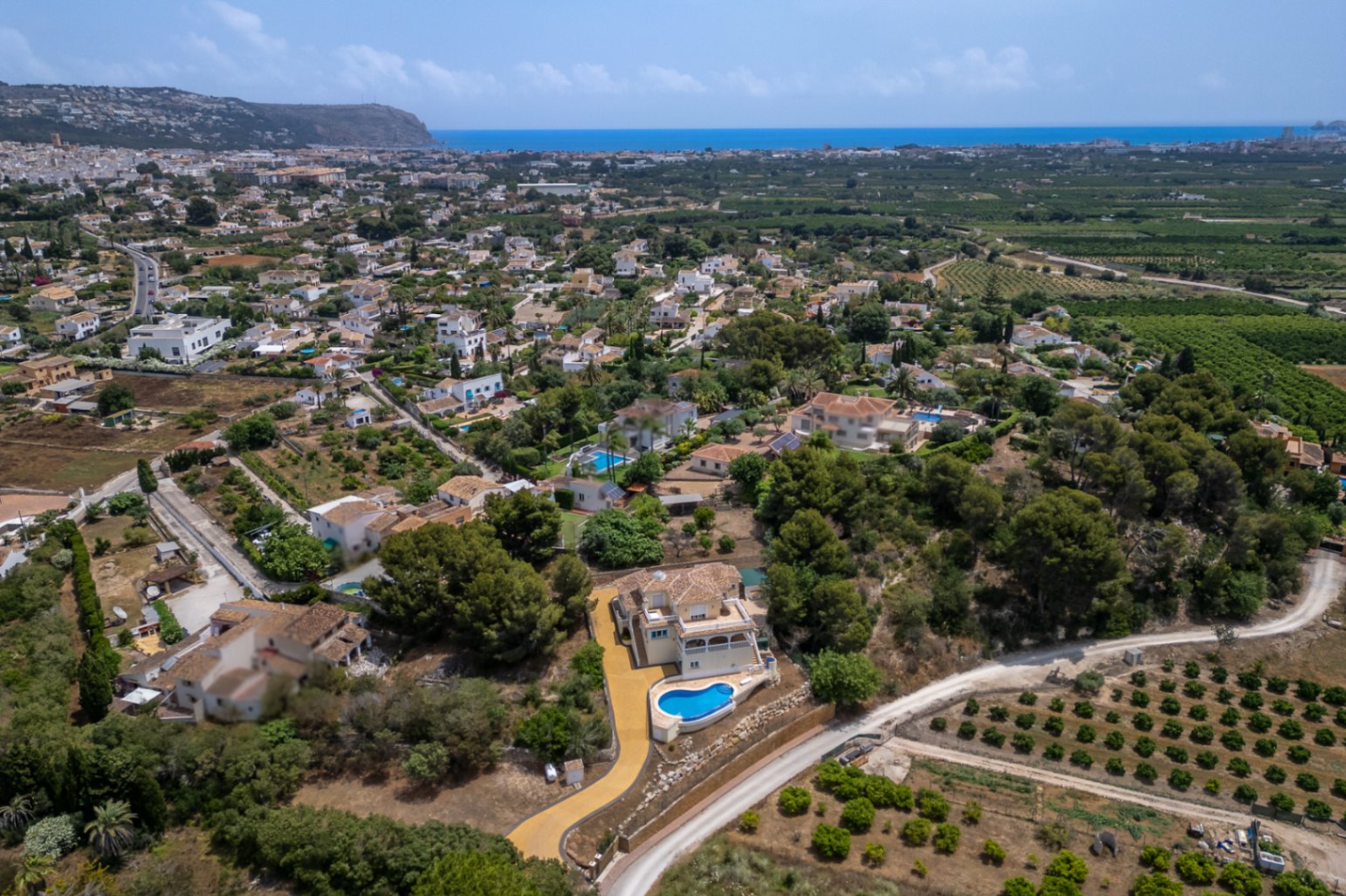 Vista aérea de la villa que resalta su ubicación elevada, con piscina infinita, amplio camino de acceso y vistas panorámicas hacia el valle de Jávea y el mar Mediterráneo.