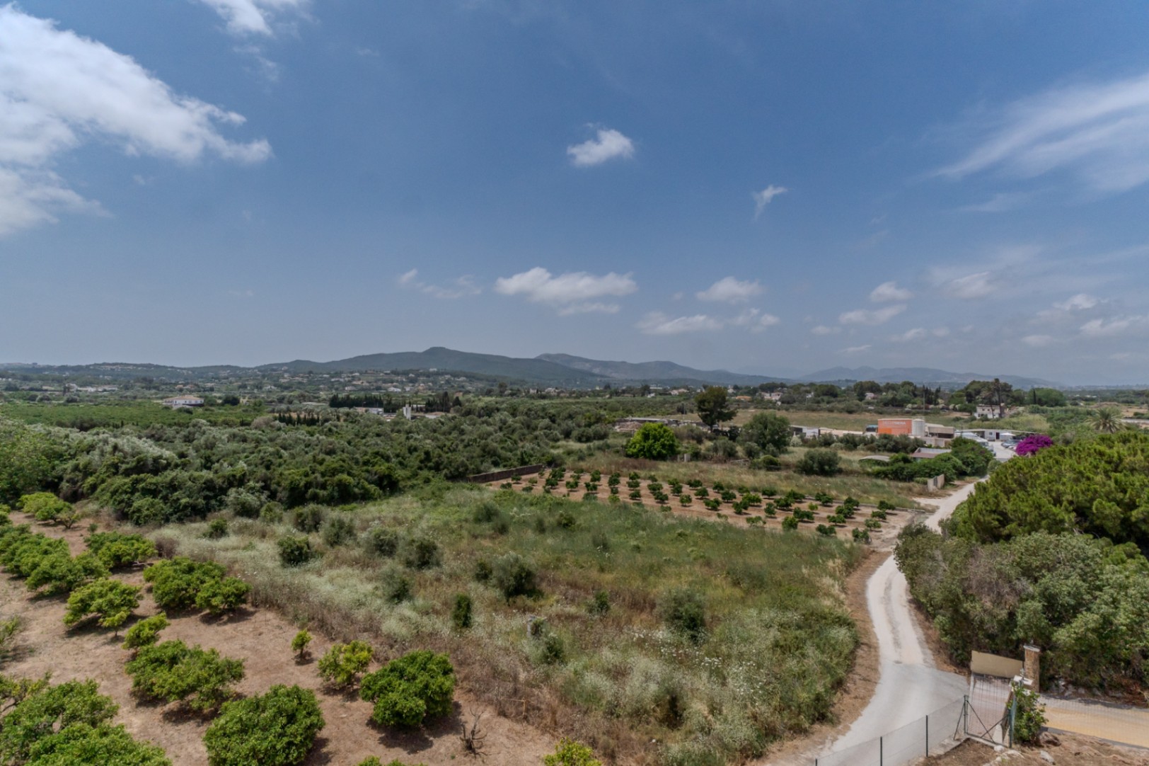 Vista panorámica de 180º desde la propiedad hacia el valle de Jávea, mostrando campos agrícolas y las colinas de Benitachell bajo un cielo despejado.