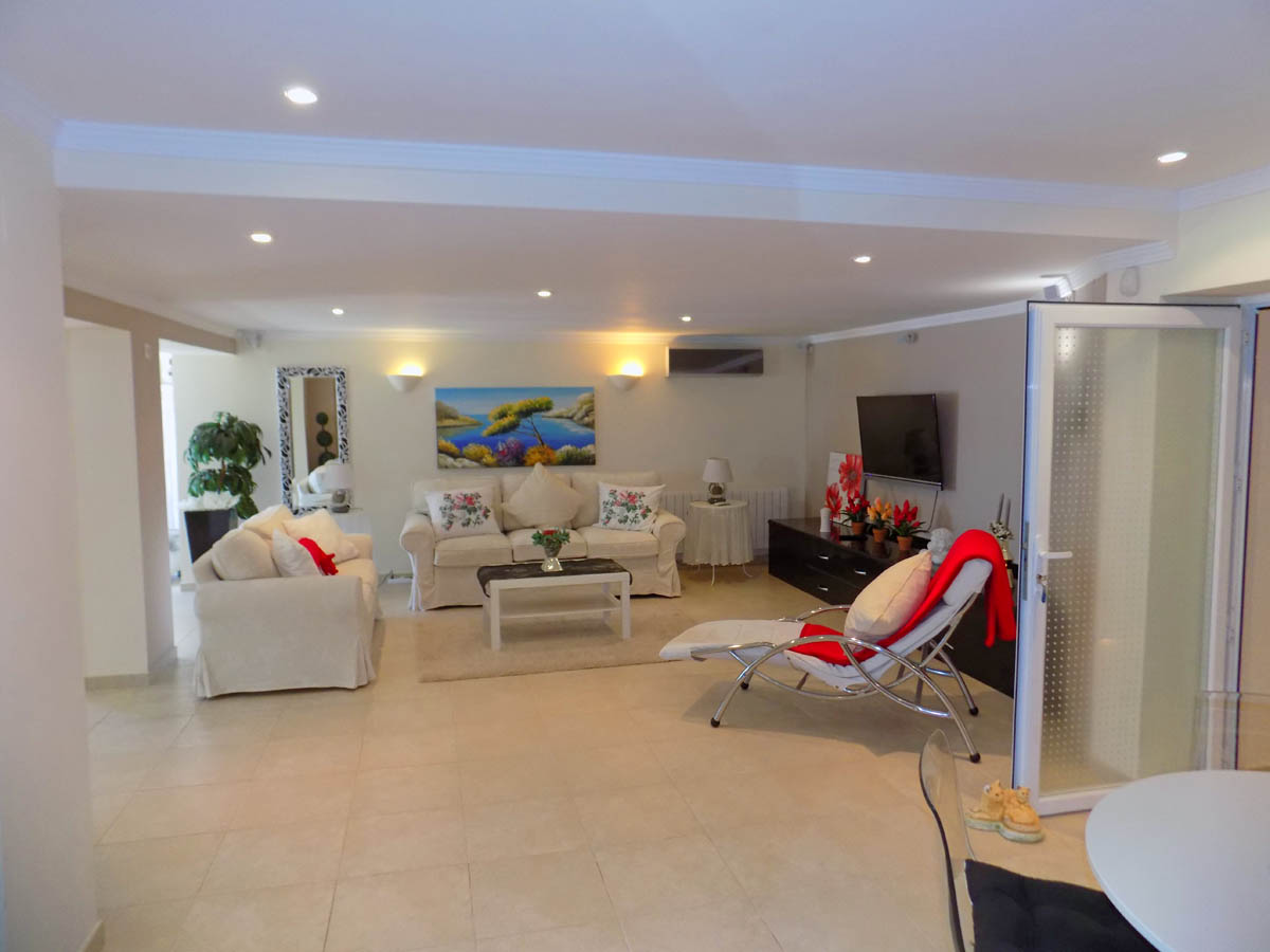 Amplio salón en la planta baja con suelos cerámicos, iluminación empotrada y zona de estar. Incluye acceso directo al exterior y un área multimedia con televisión.