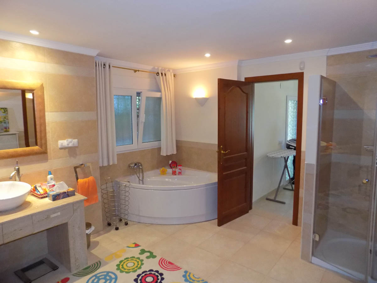 Cuarto de baño con bañera de hidromasaje de esquina, ducha independiente con mampara de cristal y encimera de piedra con lavabo sobre encimera.