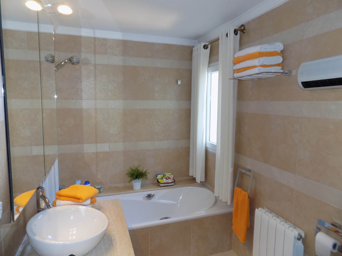 Cuarto de baño con bañera encastrada, lavabo de seno circular sobre encimera de piedra y paredes revestidas en gres de tonos crema con franjas horizontales.