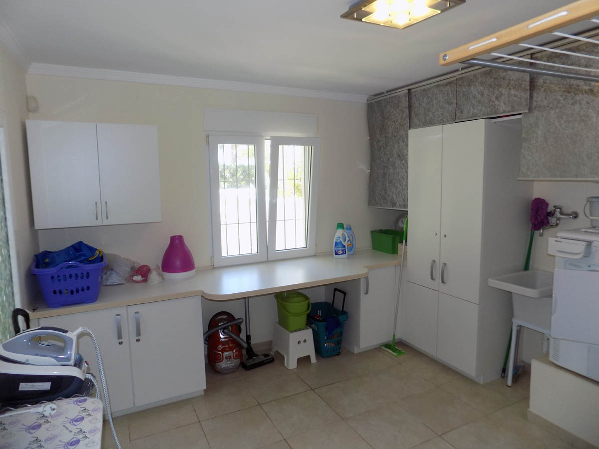 Cuarto de lavandería funcional con armarios blancos, amplia encimera, fregadero y ventana al exterior. Espacio organizado para tareas domésticas y almacenamiento.