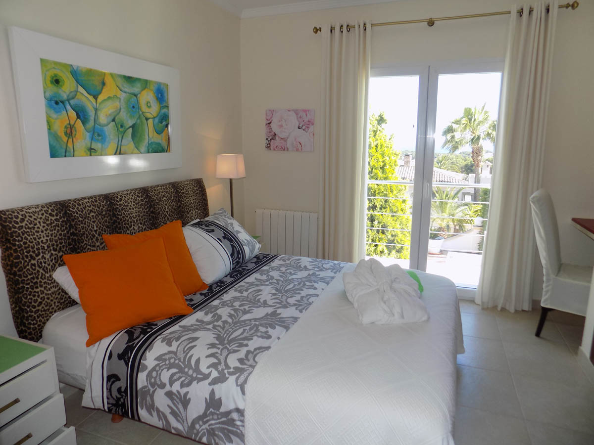 Dormitorio con cabecero de leopardo, cama doble y acceso directo a una terraza soleada con vistas a la vegetación mediterránea y palmeras.