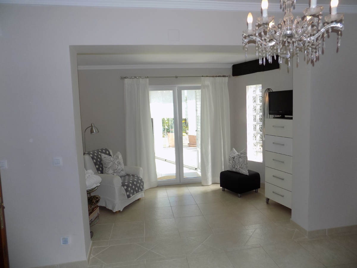 Dormitorio principal con zona de estar, suelos de gres con diseño geométrico y acceso directo a la terraza. Incluye una cómoda blanca y ventanal de bloques de vidrio.