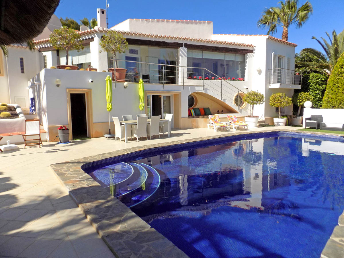 Exterior de la villa con piscina de 12m x 5,5m, amplia terraza con comedor exterior y zona chill-out integrada bajo la escalera de acceso a la planta principal.