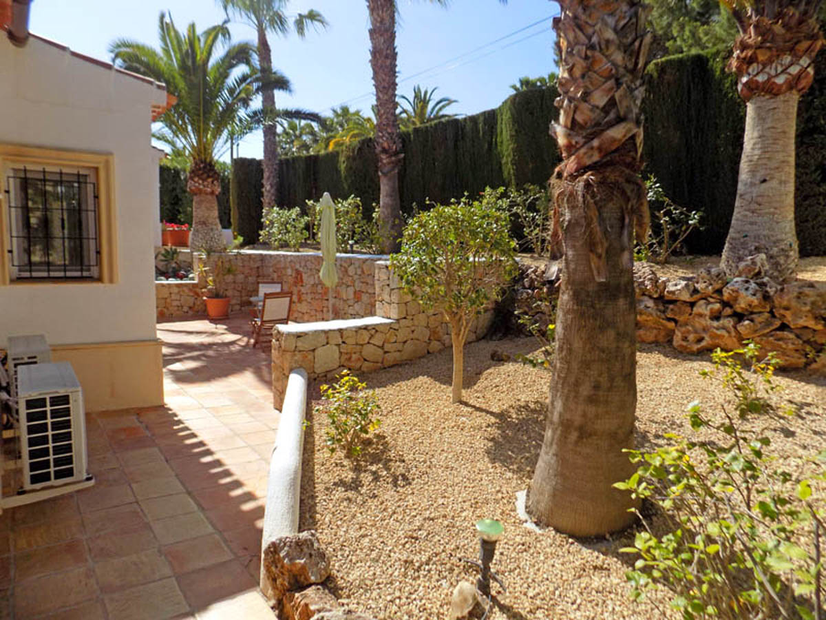 Jardín mediterráneo con palmeras maduras, muros de piedra natural y suelos de terracota. El paisajismo incluye grava y setos altos que garantizan total privacidad.
