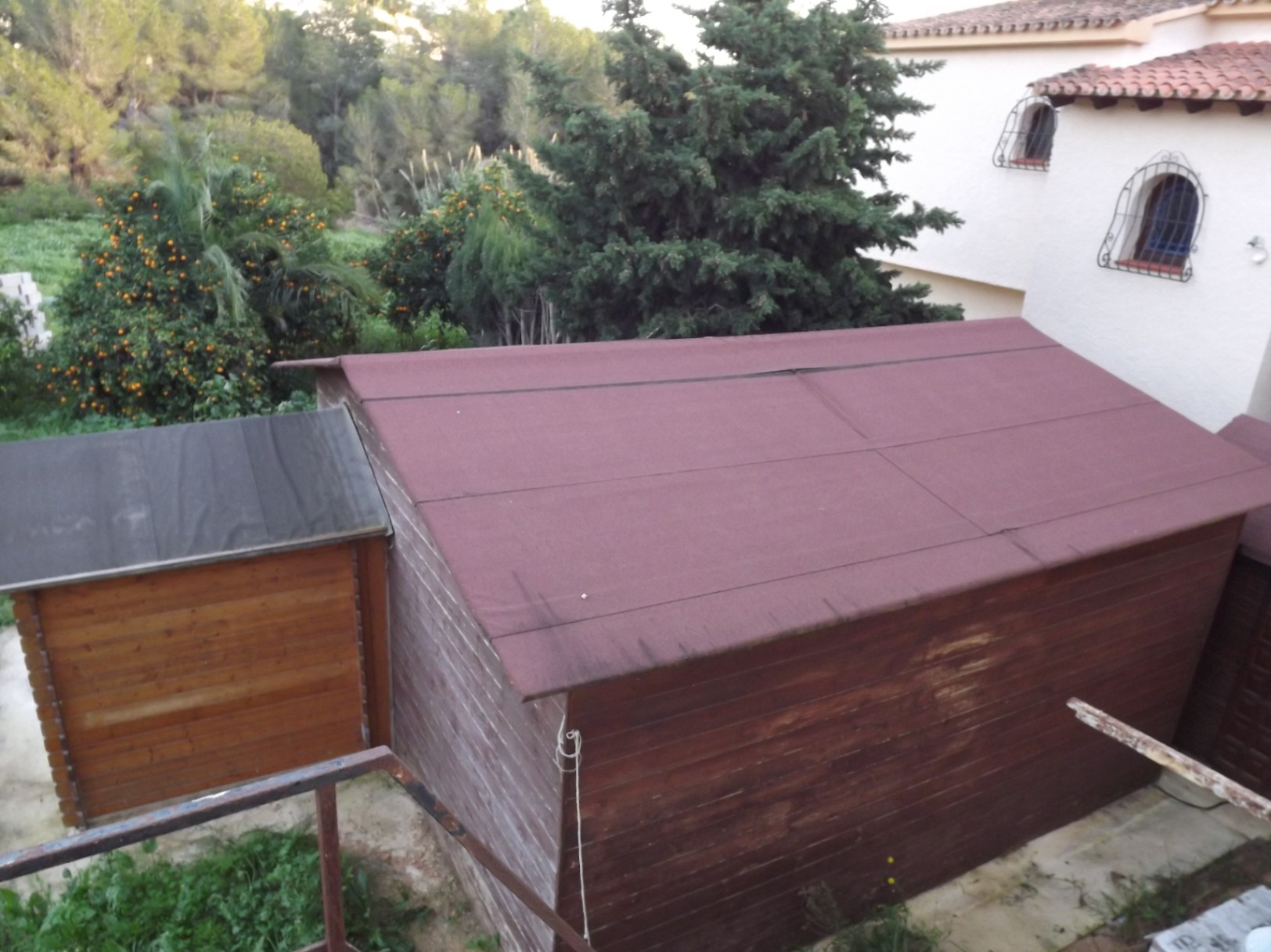 Cobertizos de madera destinados a almacenamiento, ubicados en la amplia parcela junto a árboles frutales y vegetación autóctona.
