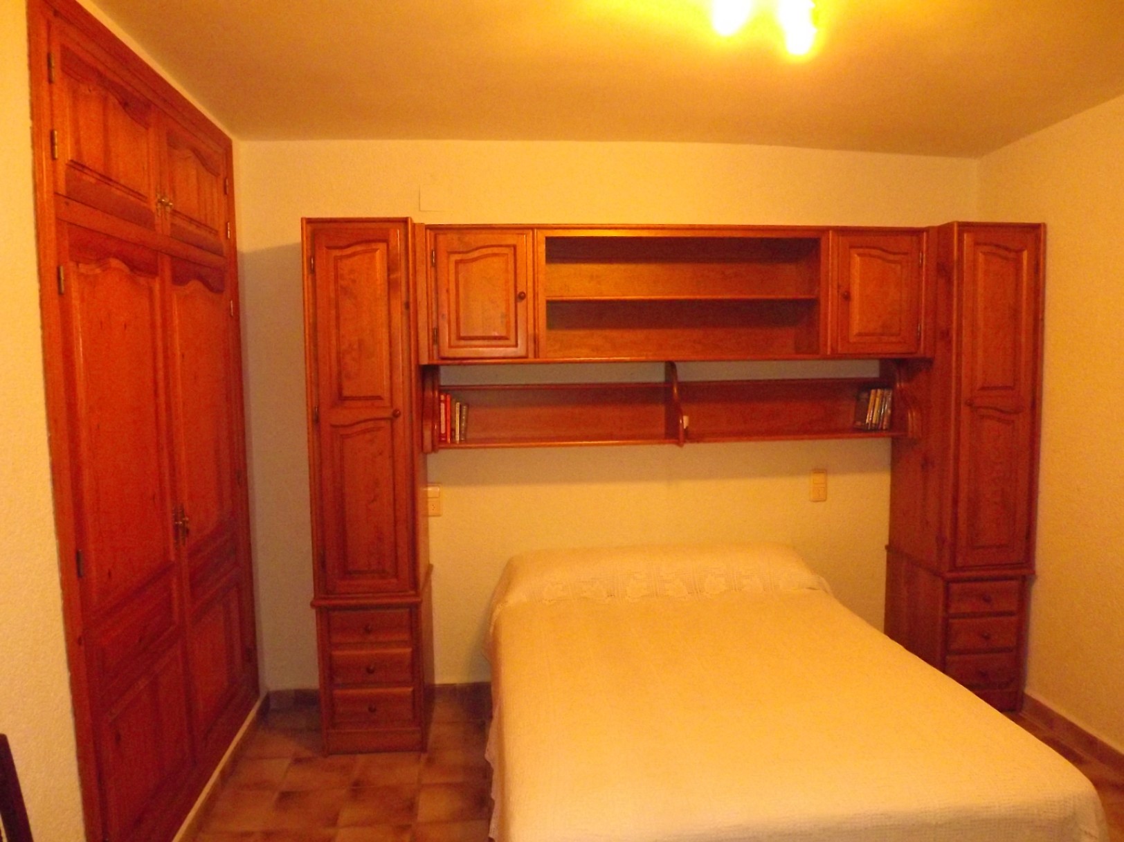 Dormitorio con mobiliario de madera maciza, incluyendo un armario empotrado y una estructura de puente con estanterías y cajoneras sobre la cama.
