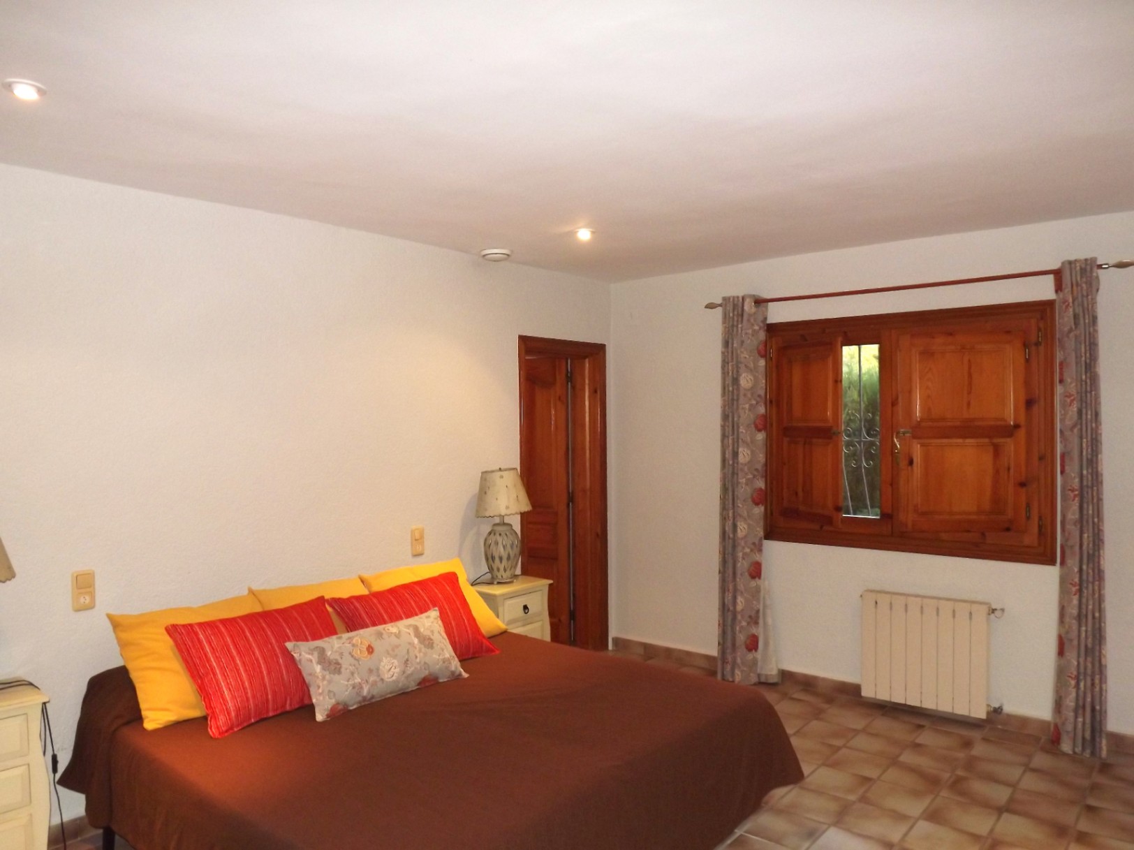 Dormitorio doble con suelos de gres, ventana de madera con contraventanas y radiador de calefacción. Incluye iluminación empotrada y carpintería interior en madera natural.