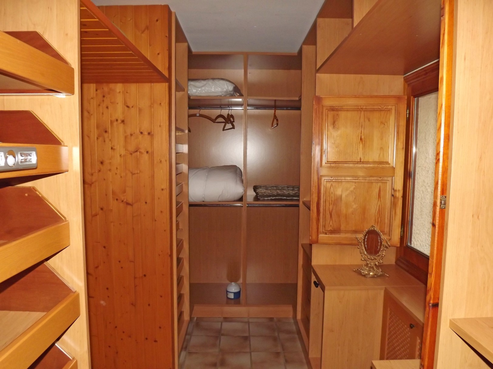 Vestidor revestido íntegramente en madera con estanterías a medida, barras para colgar y suelo cerámico. Incluye una ventana con contraventana de madera para ventilación natural.