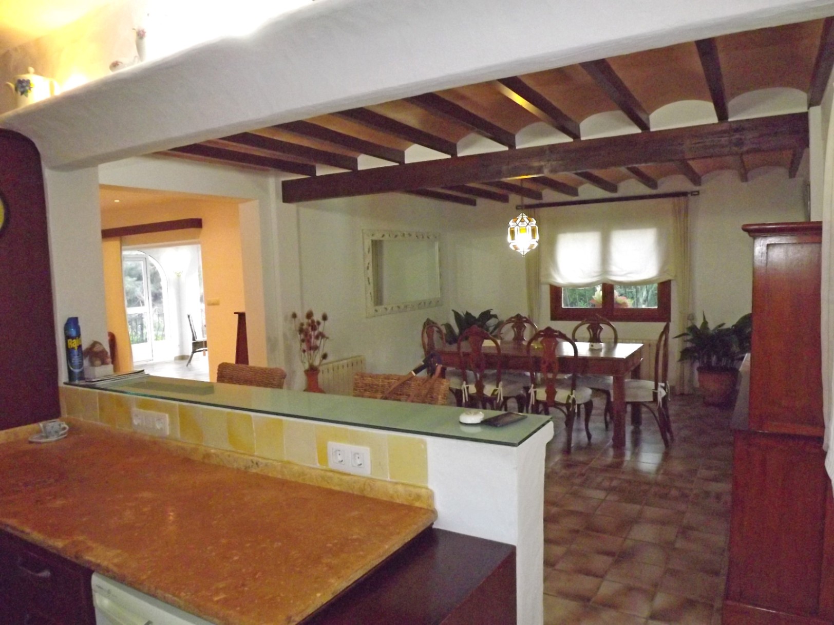 Vista desde la cocina hacia el comedor, destacando los techos con vigas de madera vista y bovedillas, suelos cerámicos y una barra de desayuno con encimera de piedra.