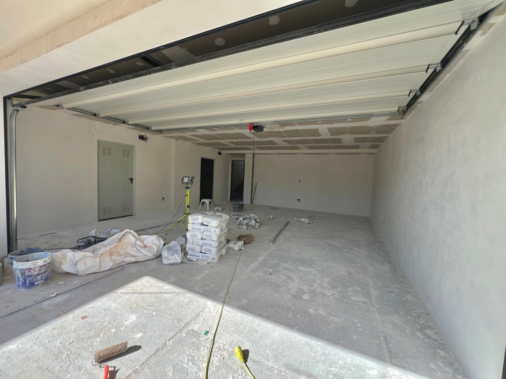 Amplio garaje en fase de construcción con puerta seccional blanca, suelos de hormigón y acceso directo a las zonas interiores de la villa.