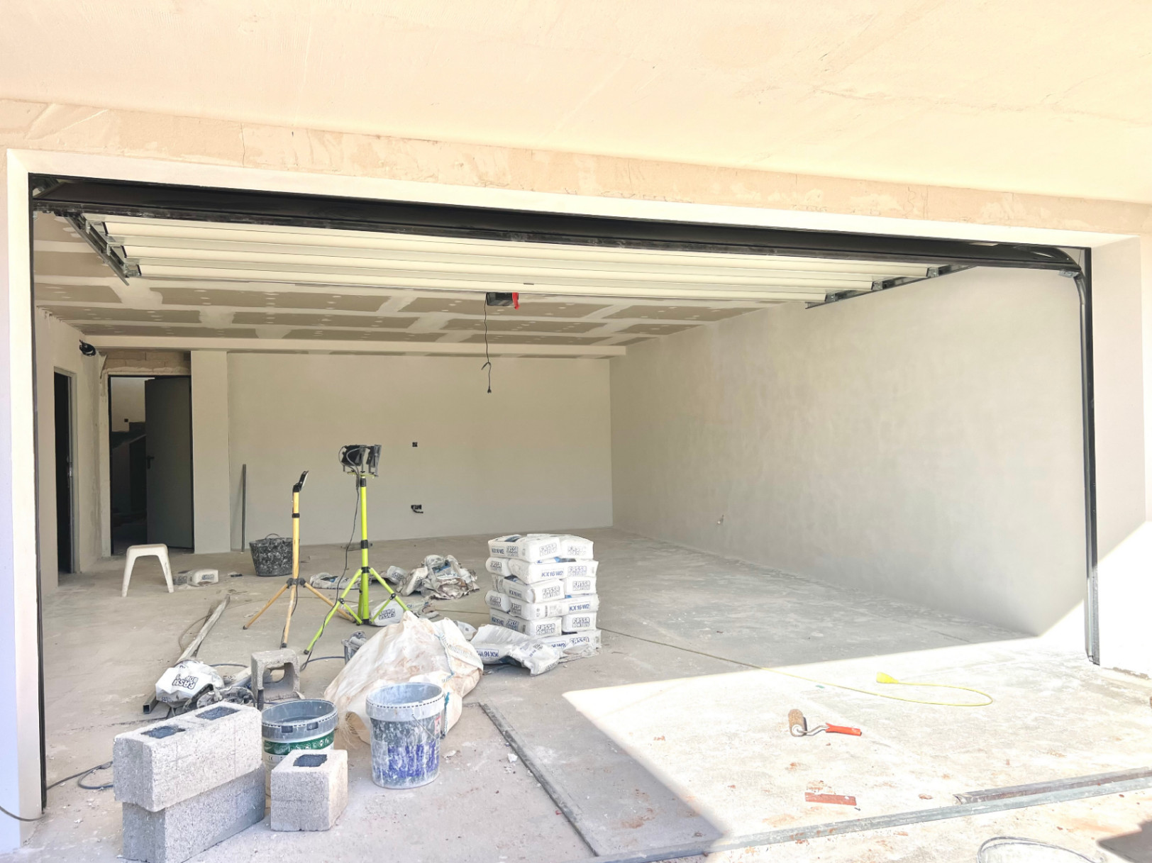 Amplio garaje en fase de construcción con puerta seccional blanca, techos de pladur y preinstalación de iluminación en una villa moderna en Jávea.