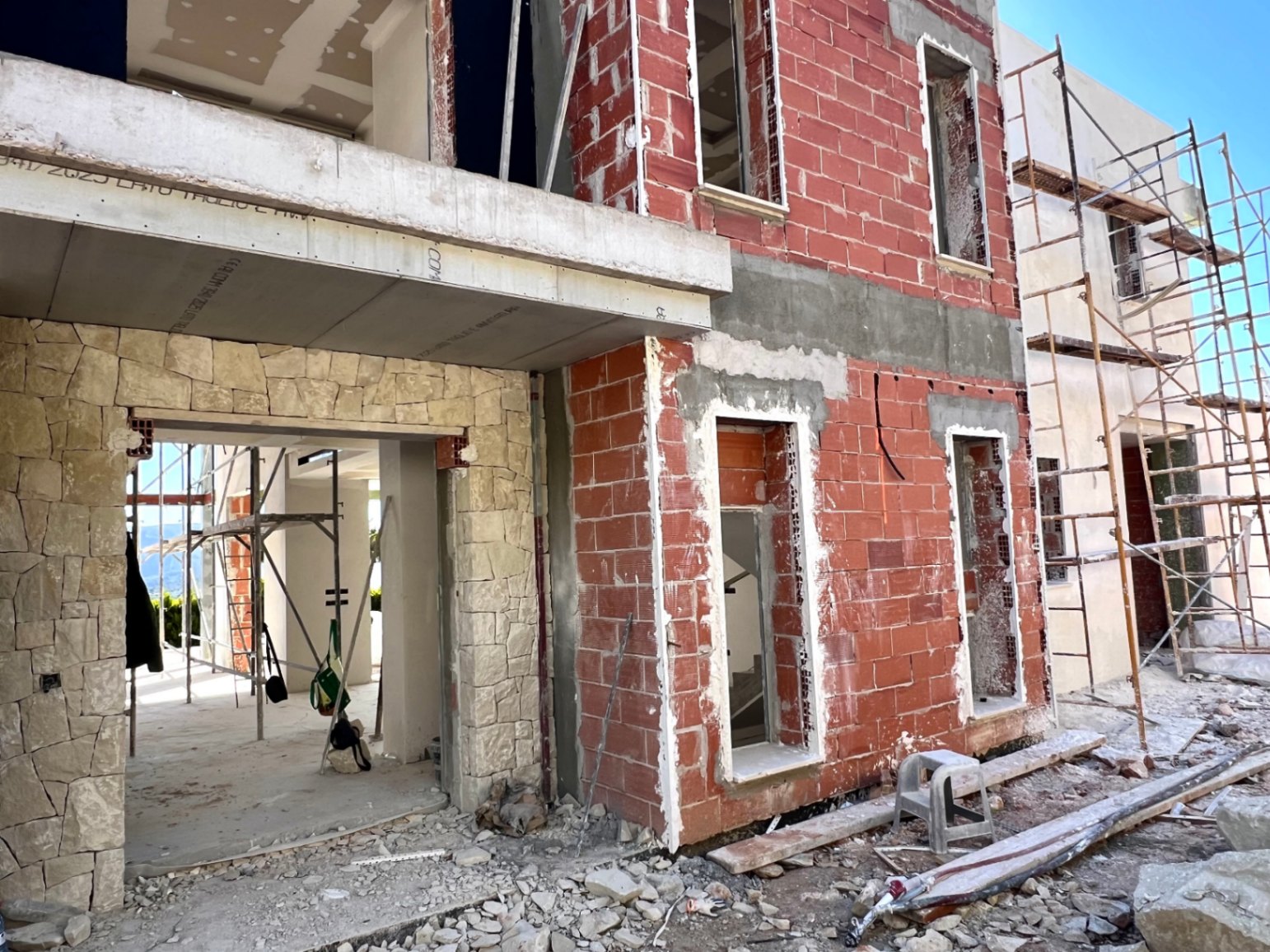 Estado actual de la construcción mostrando la fachada de ladrillo cerámico, el revestimiento de piedra natural y los amplios huecos para ventanales.