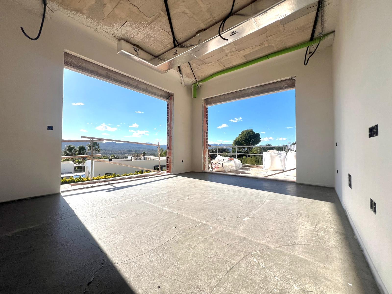 Interior en fase de construcción con amplios ventanales, techos de hormigón con preinstalación de climatización y vistas despejadas al valle.