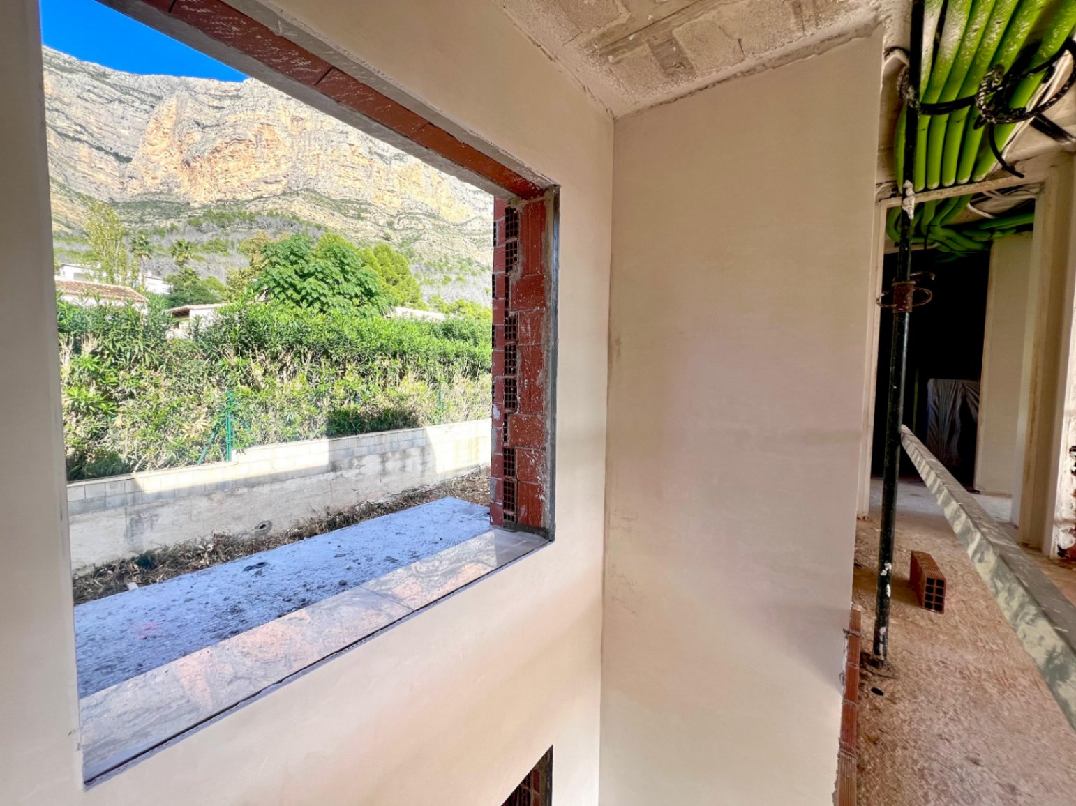 Vista desde el interior en construcción hacia el macizo del Montgó, mostrando el cerramiento de ladrillo y las instalaciones técnicas en el techo.