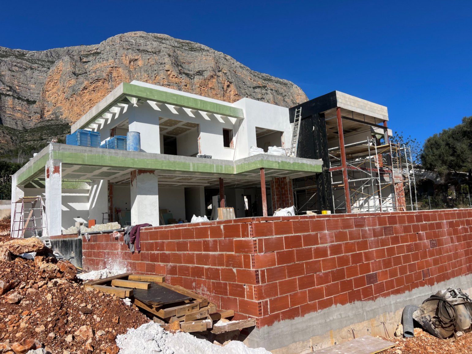 Vista exterior de la villa en fase de construcción con el macizo del Montgó al fondo, destacando la estructura de dos niveles y las amplias zonas de terrazas.