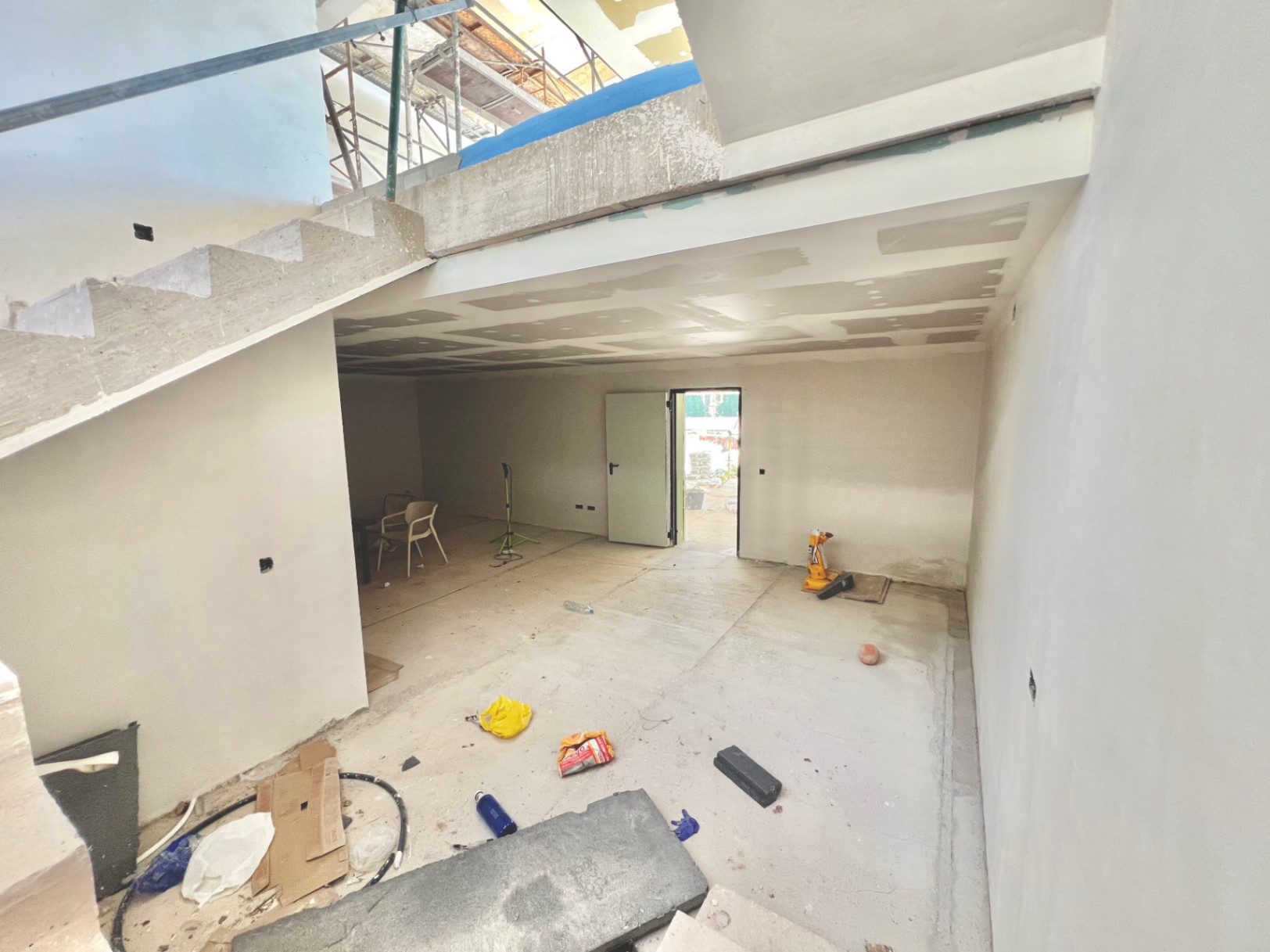 Vista interior de la planta inferior en construcción, con escalera de hormigón y espacio diáfano destinado a zona polivalente o gimnasio.