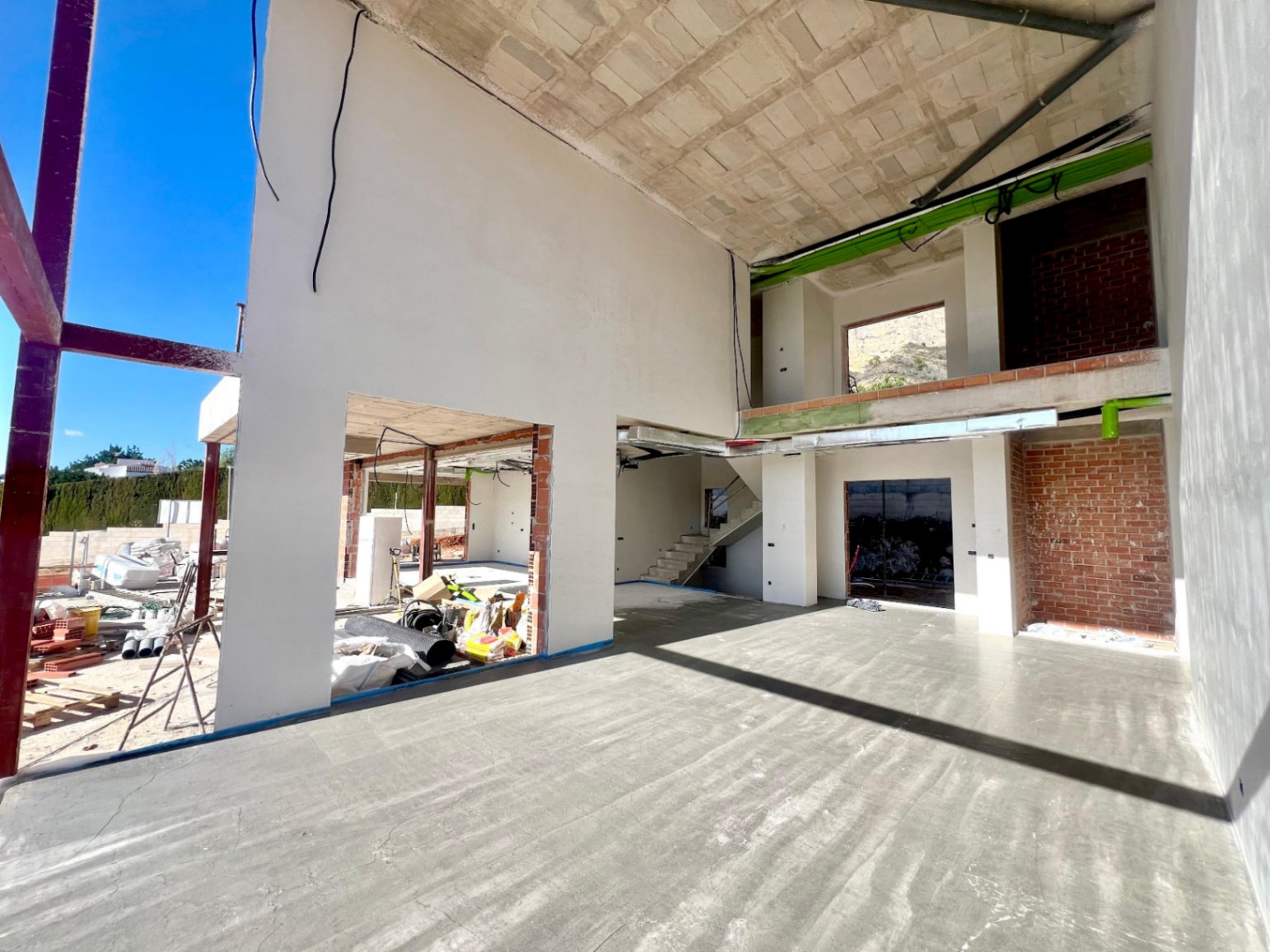 Vista interior del salón a doble altura en construcción, destacando el altillo abierto, la escalera de hormigón y los grandes huecos para ventanales de suelo a techo.