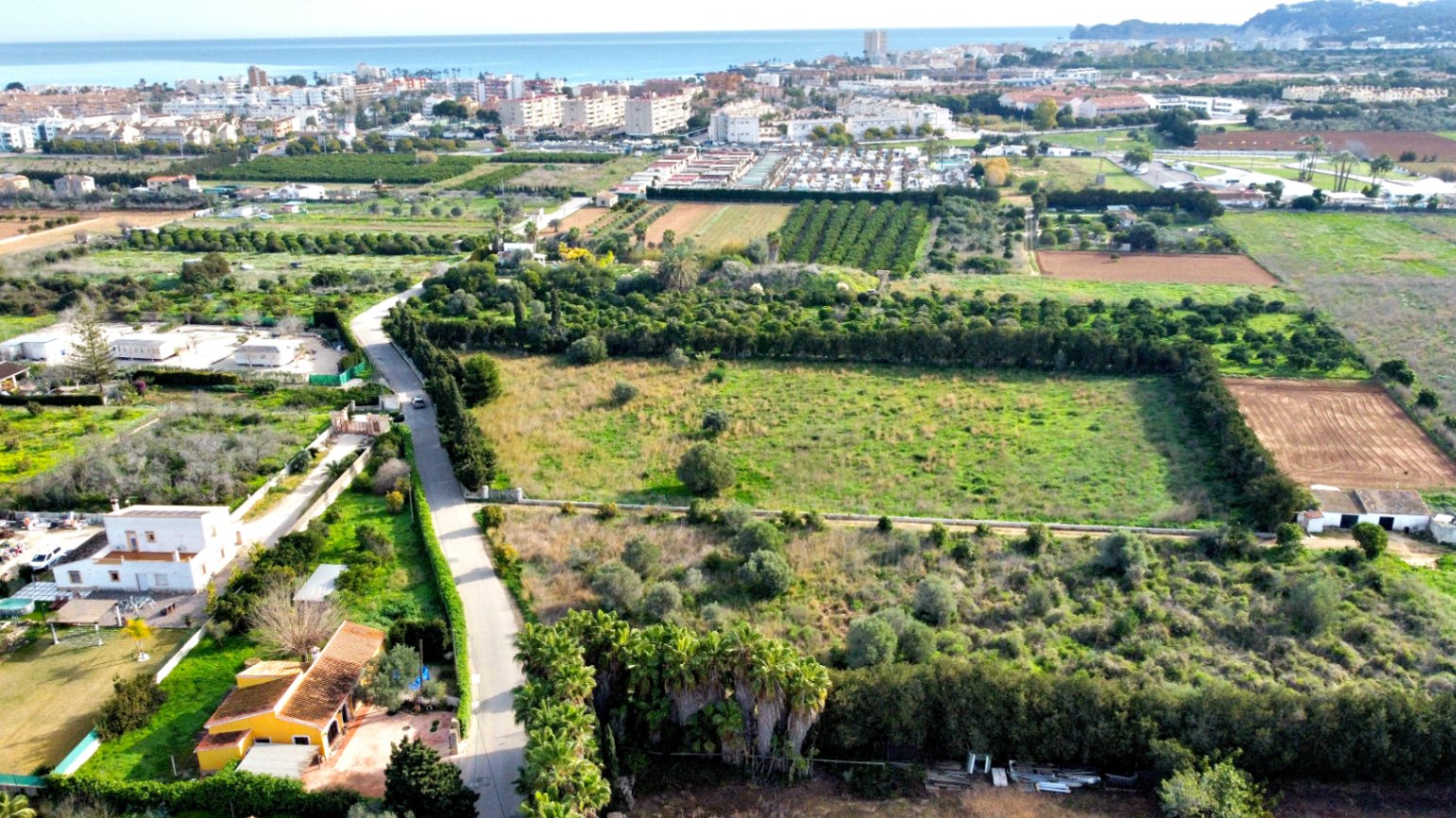 Vista aérea de la amplia parcela rodeada de setos y campos, con vistas despejadas hacia el mar Mediterráneo y el núcleo urbano costero.