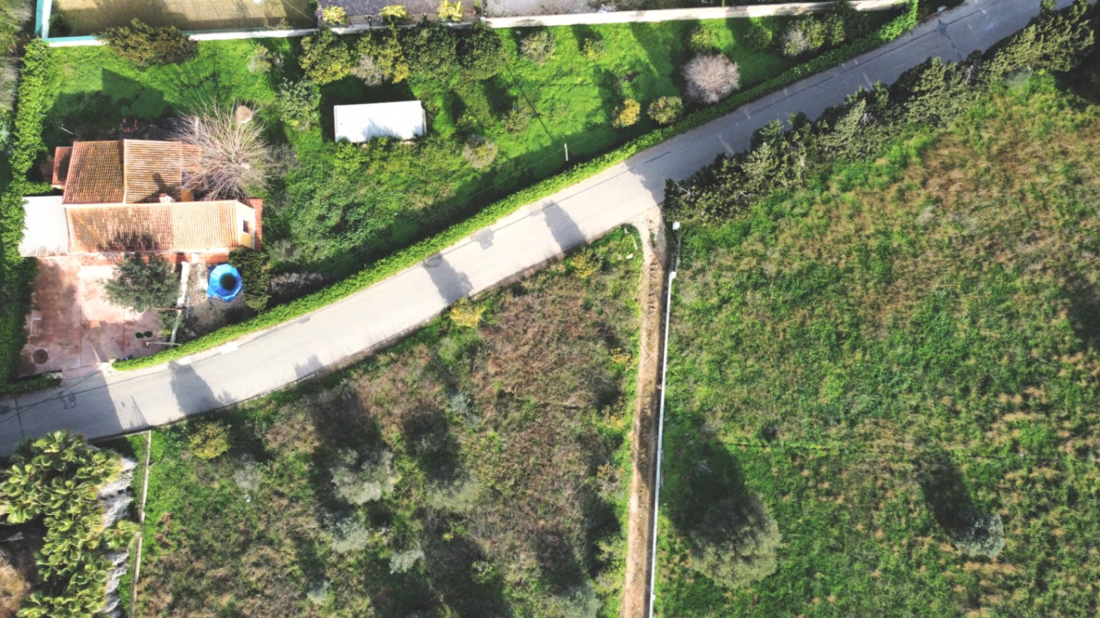 Vista aérea de la propiedad que muestra la casa de teja cerámica, la amplia parcela de 1.414 m² con vegetación autóctona y el acceso por camino asfaltado.