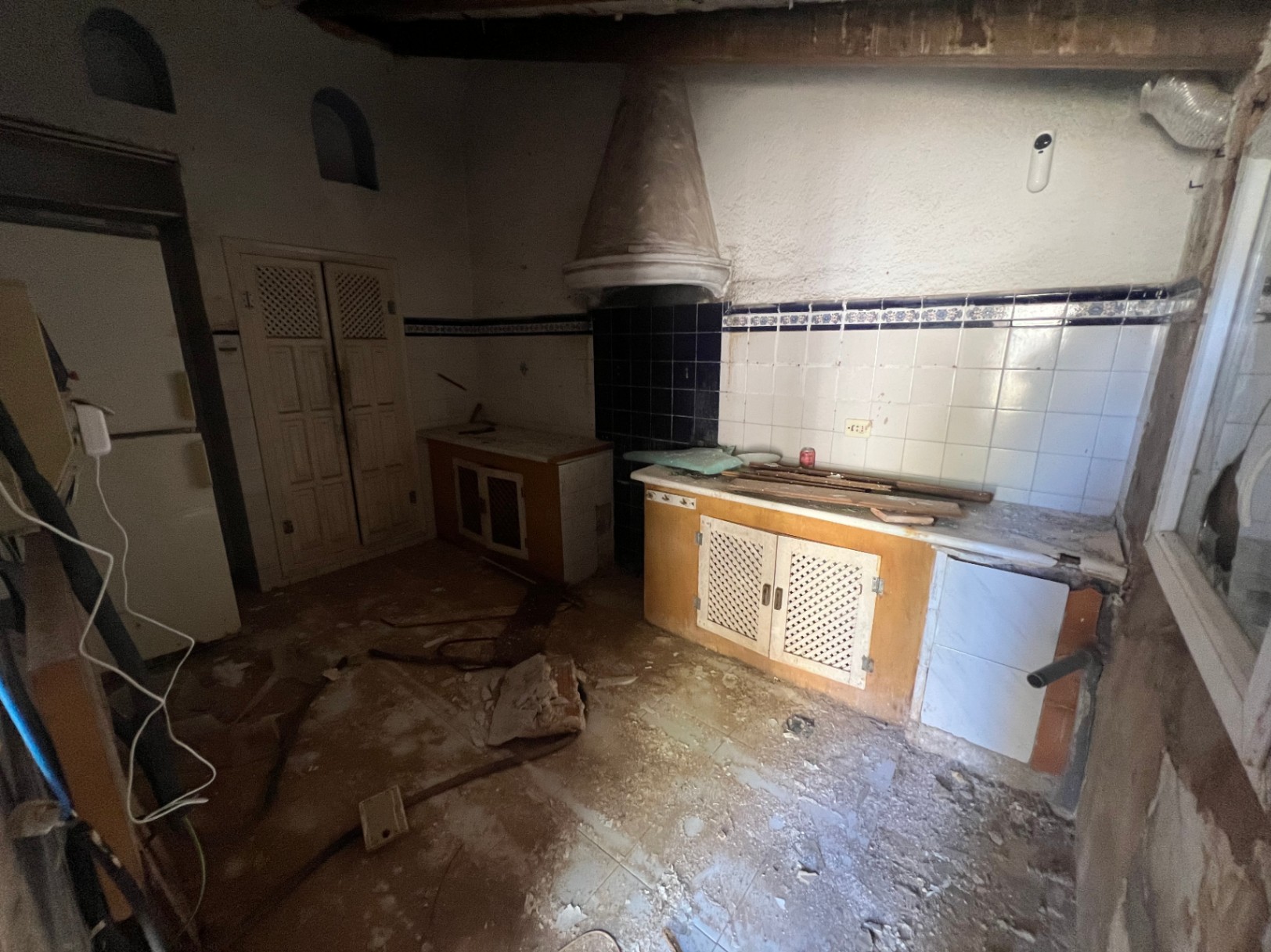 Cocina original para reformar con campana extractora cónica, azulejos blancos con cenefa azul y armarios de madera con celosía. Espacio con vigas vistas y gran potencial.