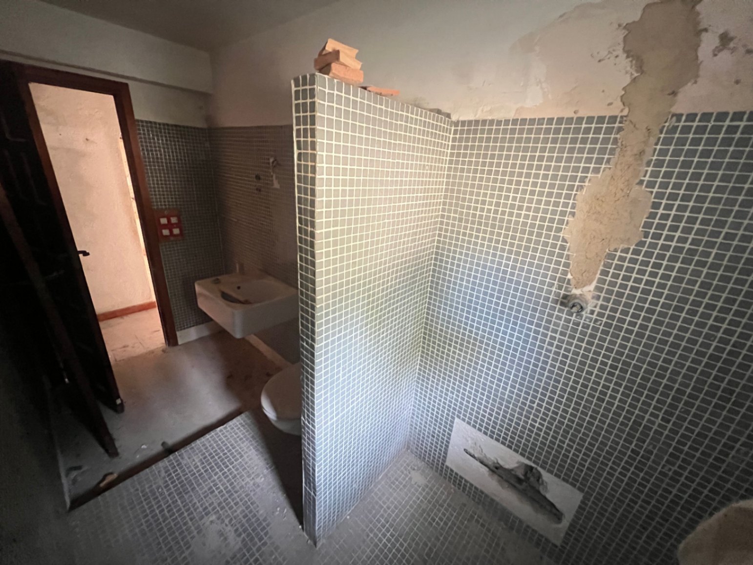 Cuarto de baño original con azulejos de gresite azul, lavabo y sanitario. El espacio requiere una reforma integral para modernizar sus instalaciones y acabados.