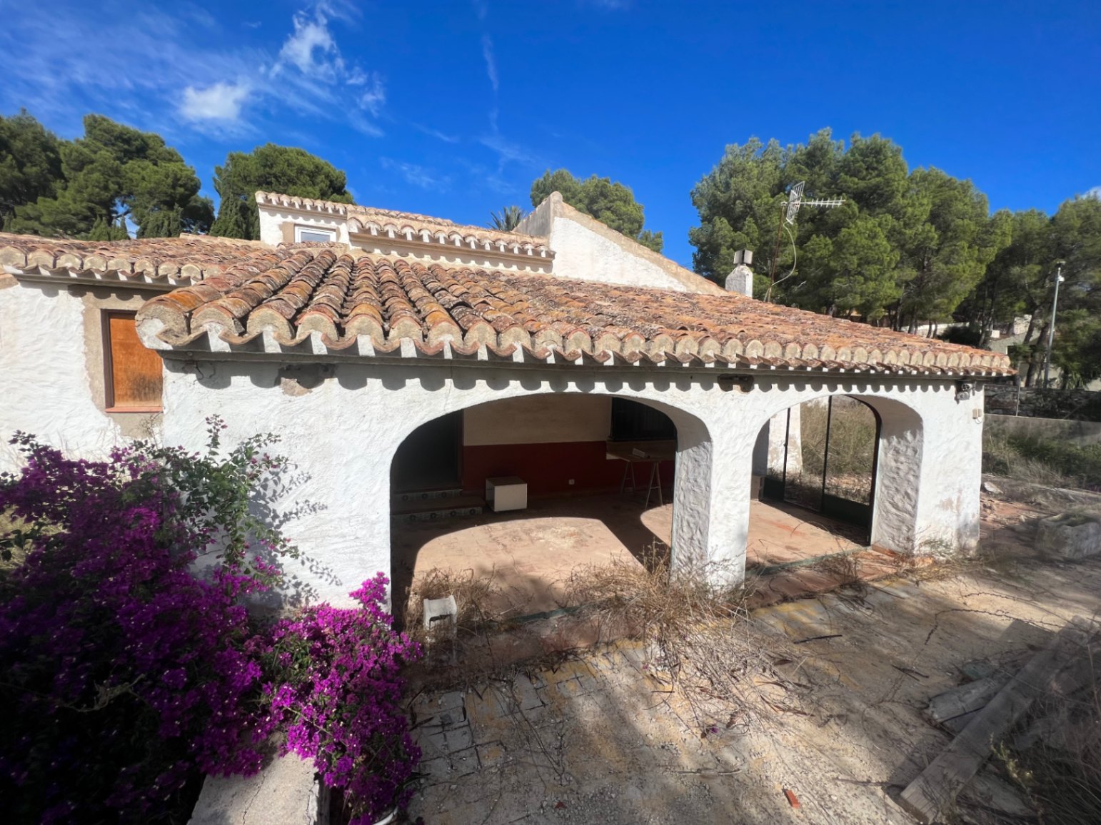Fachada exterior con naya tradicional de arcos, tejado de teja cerámica y buganvilla. La estructura muestra el estilo mediterráneo clásico listo para ser reformado.