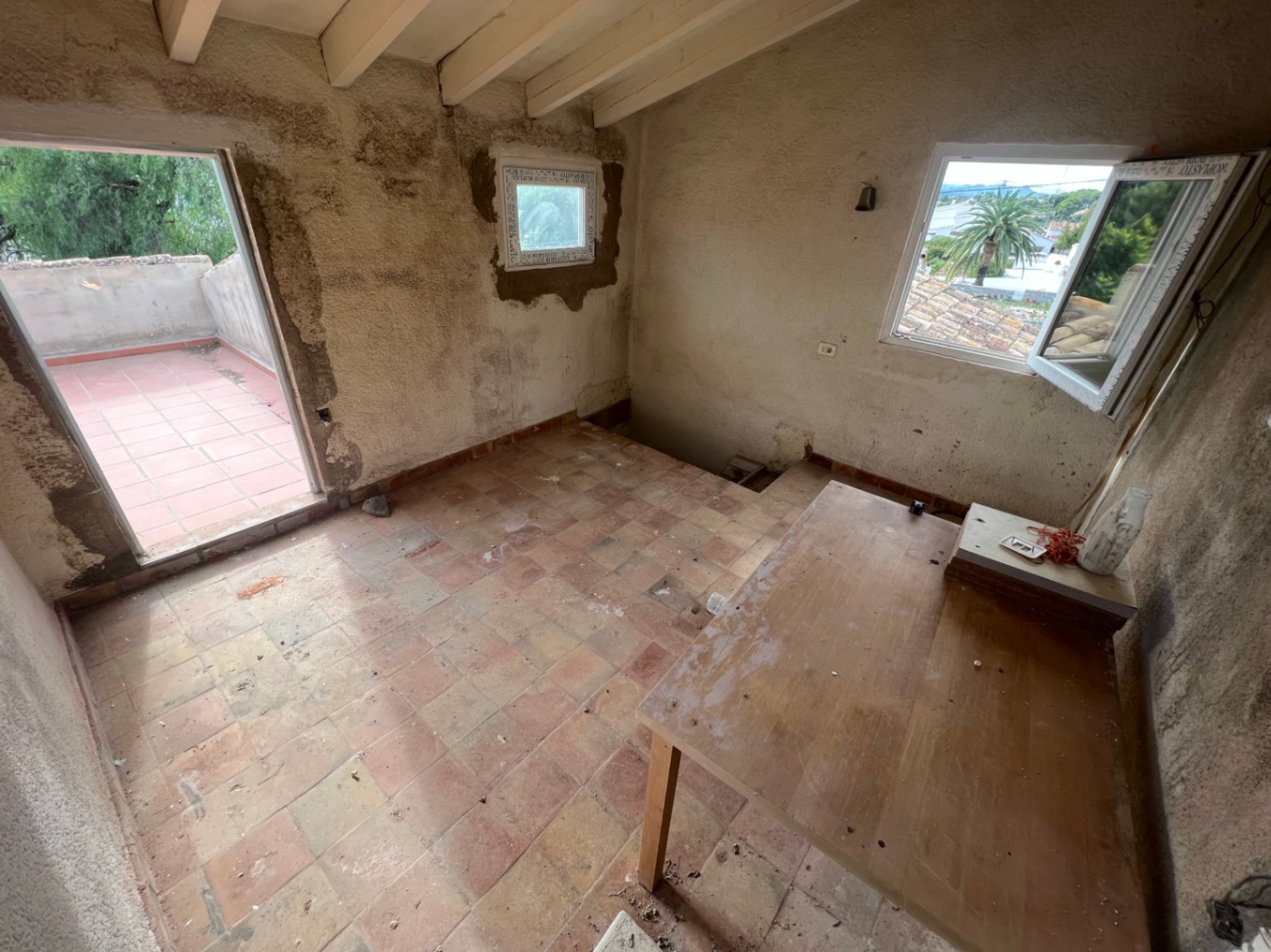 Habitación en planta superior con vigas de madera a la vista, suelos de terracota y acceso directo a una terraza privada con vistas despejadas.