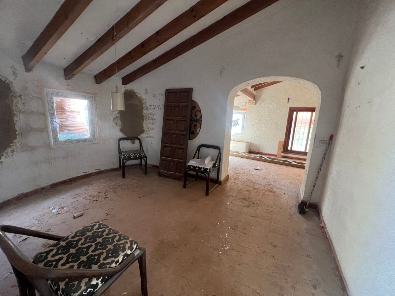 Habitación interior para reformar con techos de vigas de madera vistas, suelos de barro y un arco de paso hacia la estancia contigua.