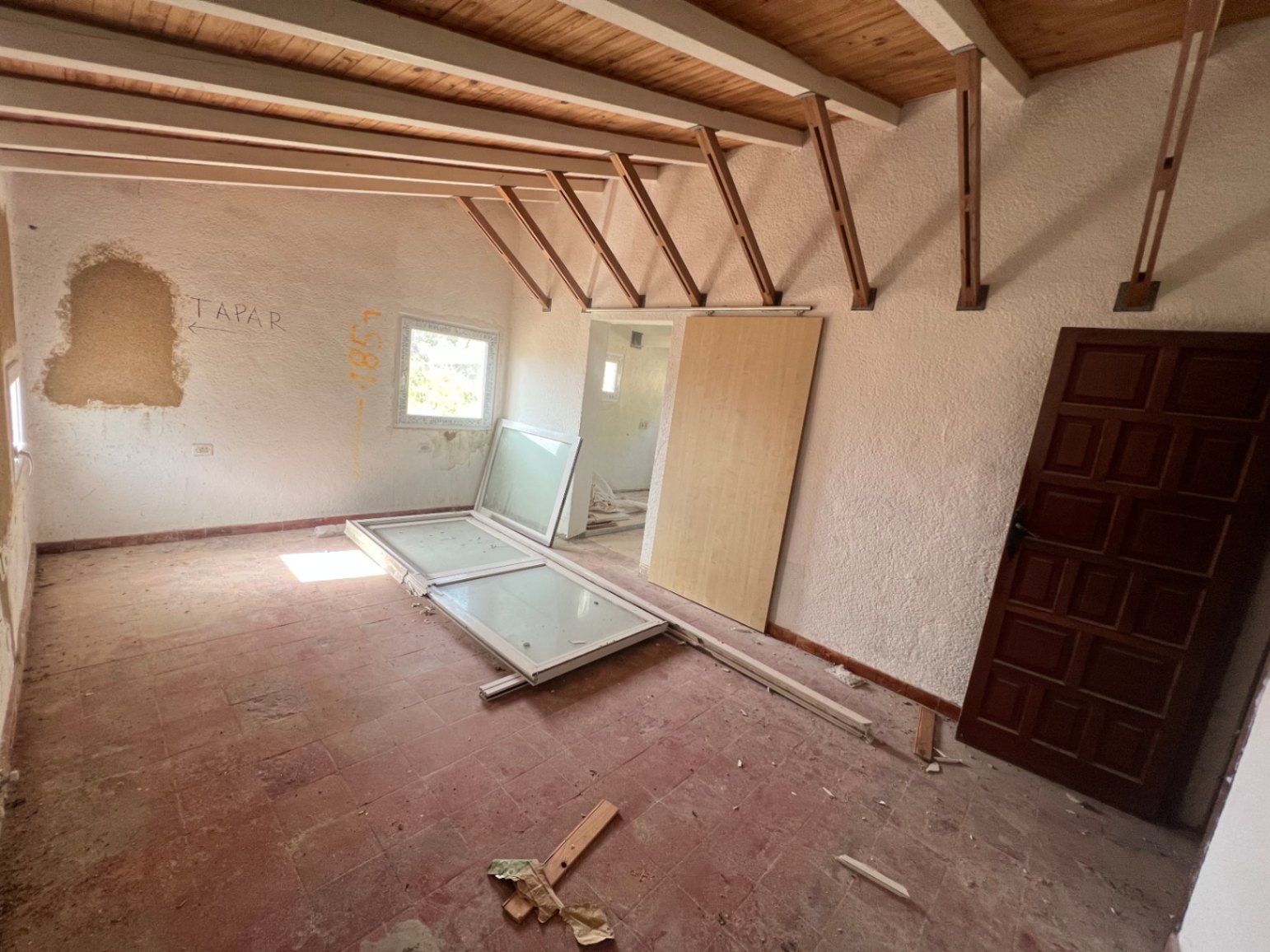Habitación para reformar con techos de vigas de madera vistas, suelos de terracota y paredes texturizadas. Espacio diáfano con gran potencial de personalización.