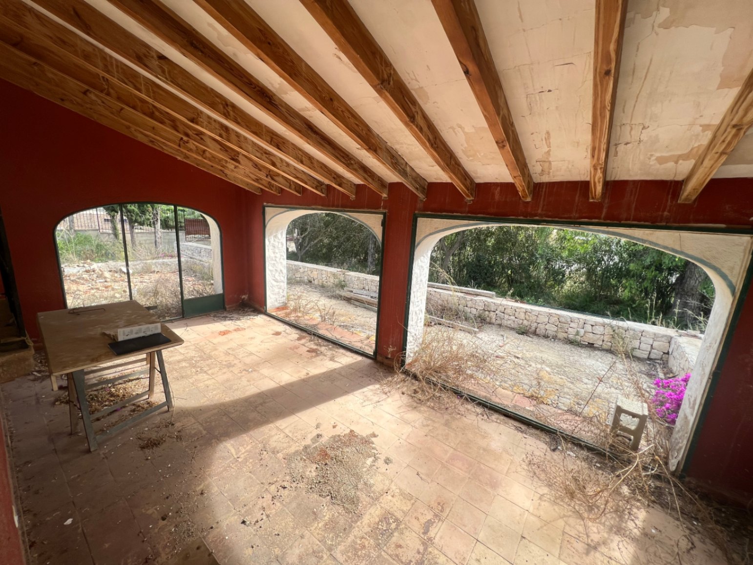 Naya cubierta con vigas de madera a la vista y suelos de terracota. Los amplios arcos ofrecen vistas al jardín y muros de piedra originales, un espacio ideal para reformar.