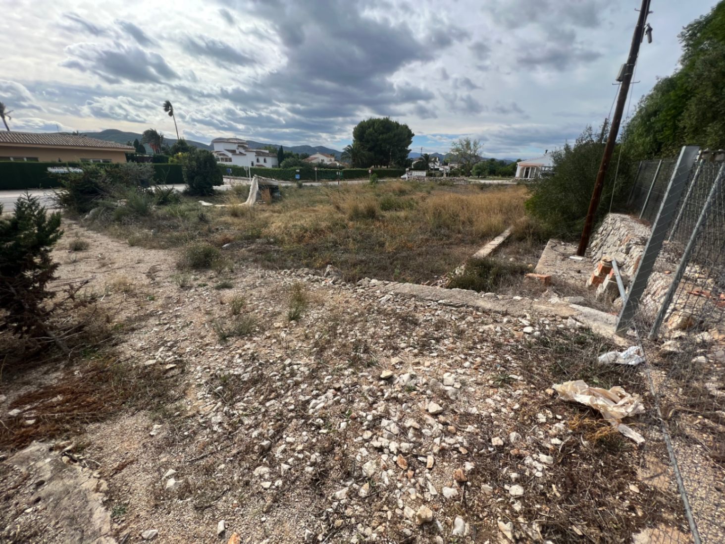 Parcela de 2.895m2 con vegetación natural, terreno llano y muros de piedra perimetrales, ofreciendo vistas despejadas a las montañas y villas colindantes en Jávea.