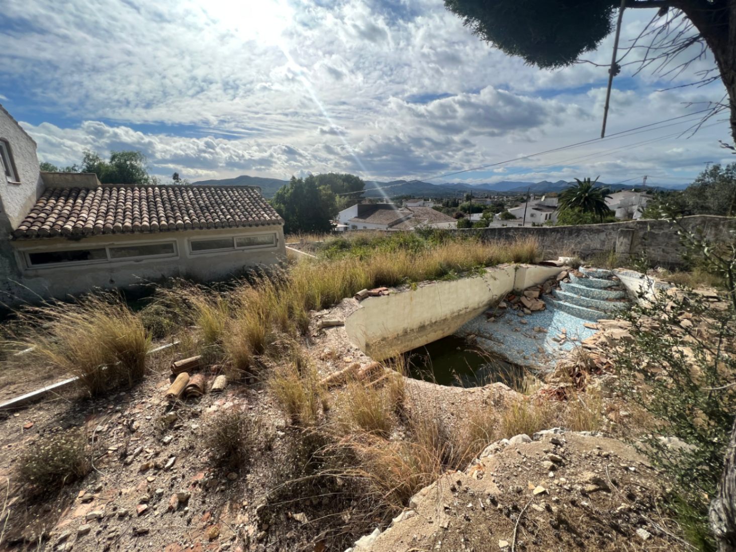 Piscina para reformar rodeada de vegetación natural, con vistas despejadas a las montañas y una construcción anexa con tejado de teja tradicional.