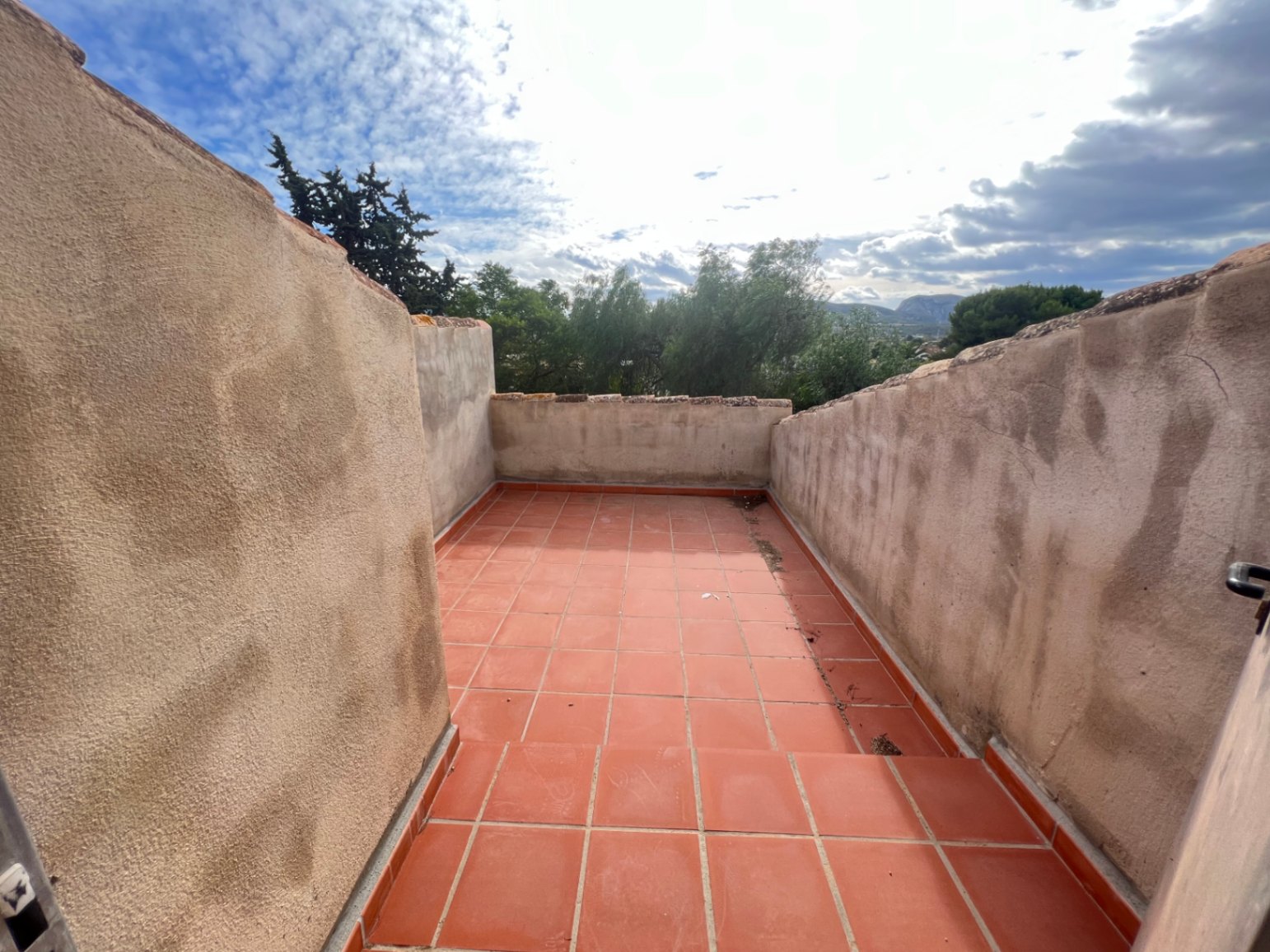Terraza superior con suelo de baldosas de terracota y muros altos, ofreciendo vistas despejadas hacia la vegetación circundante y el horizonte montañoso de Jávea.