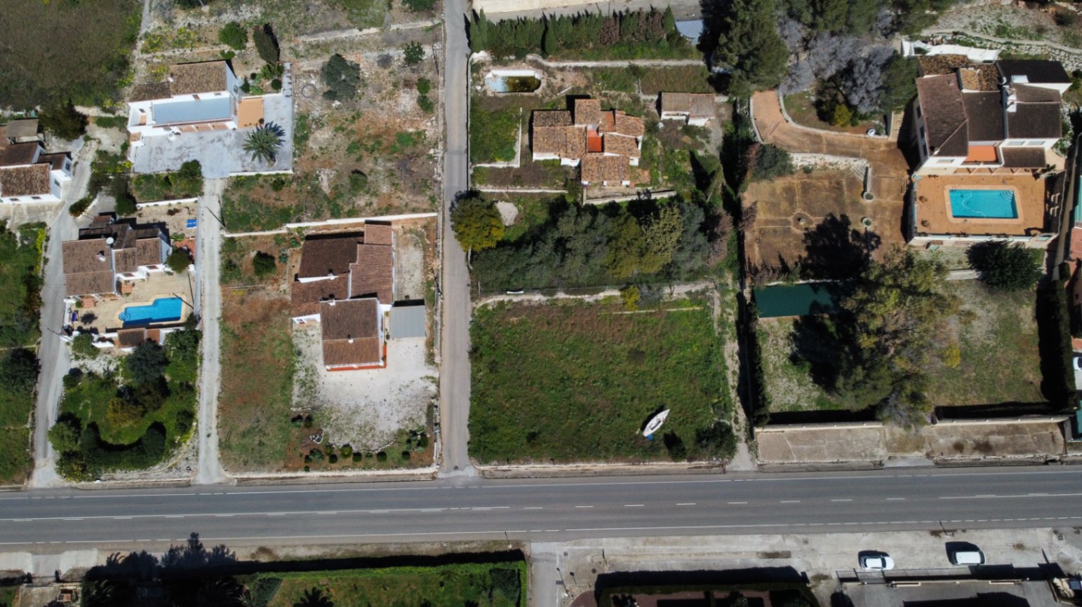 Vista aérea cenital de la extensa parcela de 2.895m2 en Jávea, mostrando la ubicación de la vivienda, el acceso directo por carretera y la amplitud del terreno disponible.