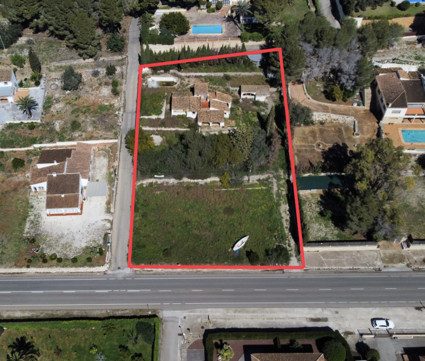 Vista aérea perimetrada de la parcela de 2.895m2 en Jávea, mostrando la vivienda principal, construcciones anexas y el amplio terreno frontal con acceso desde la carretera.