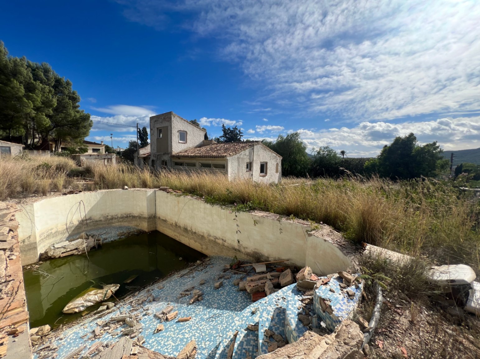 Vista exterior de la parcela con piscina para reformar y fachada de la vivienda de estilo tradicional bajo el sol del Montgó.