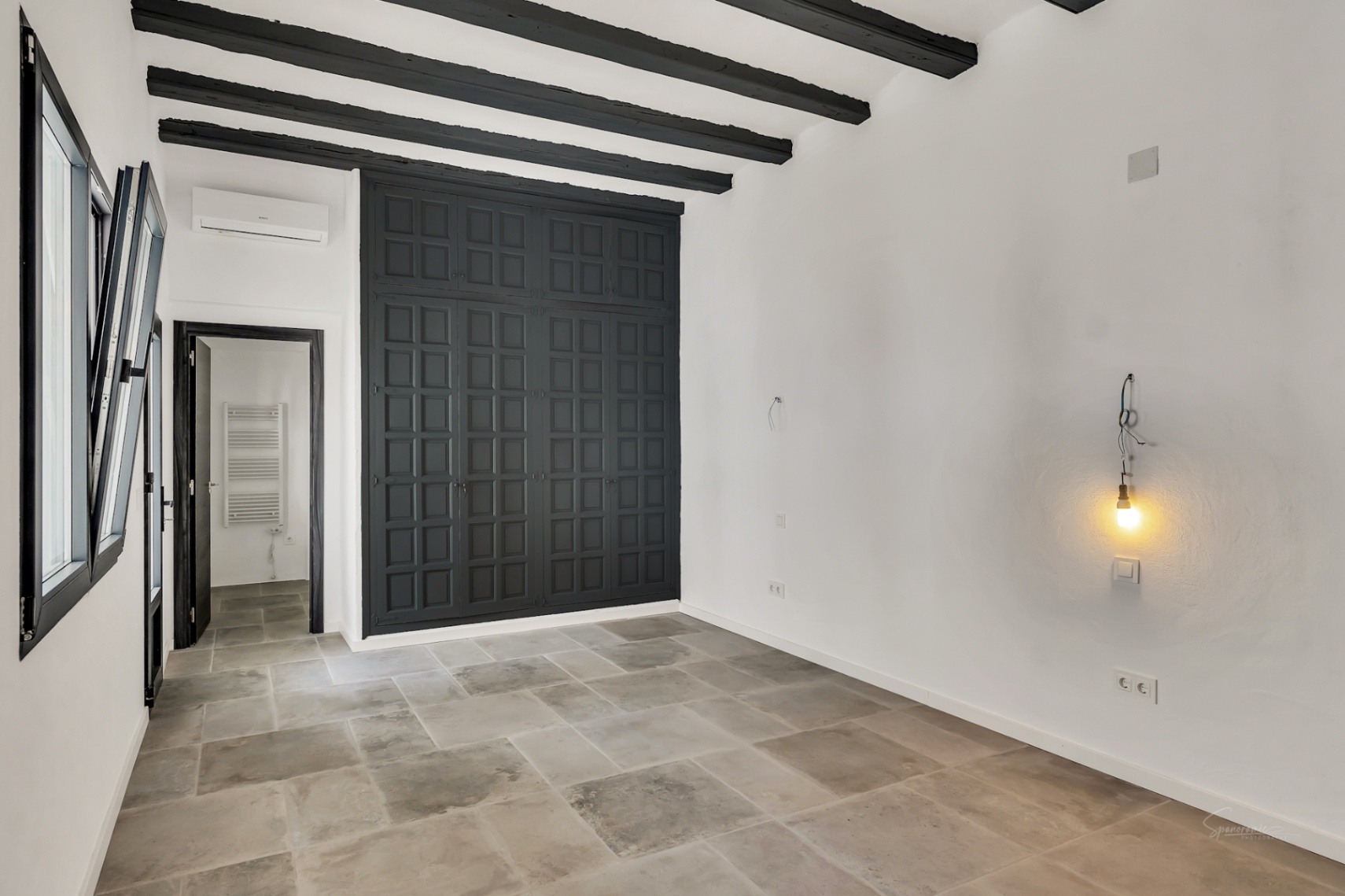 Dormitorio con vigas de madera oscura expuestas, suelos de piedra natural y un gran armario empotrado gris antracita con diseño de paneles tradicionales.