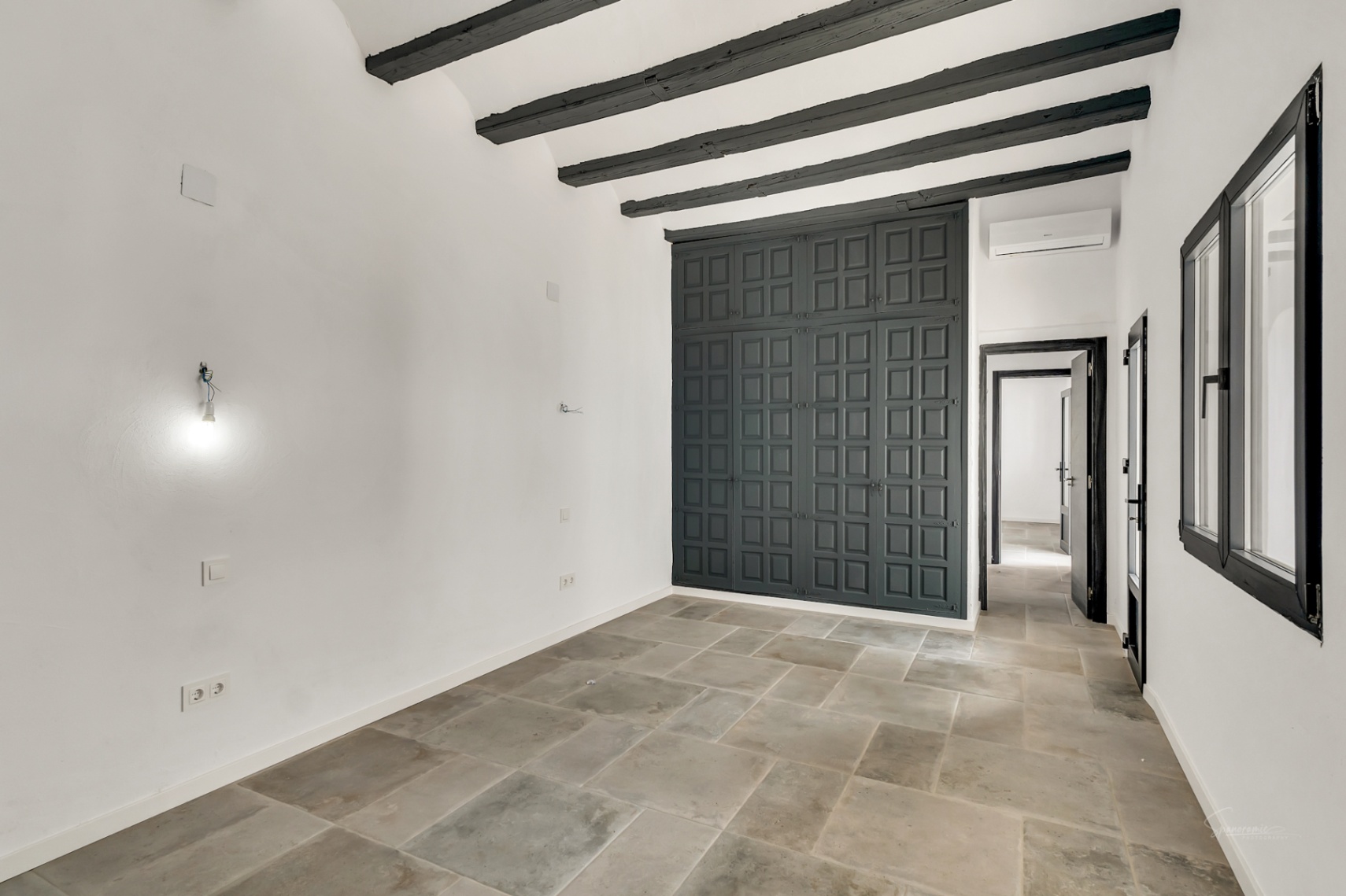 Dormitorio con vigas de madera oscura, suelos de piedra natural y un gran armario empotrado de diseño clásico en color gris antracita.
